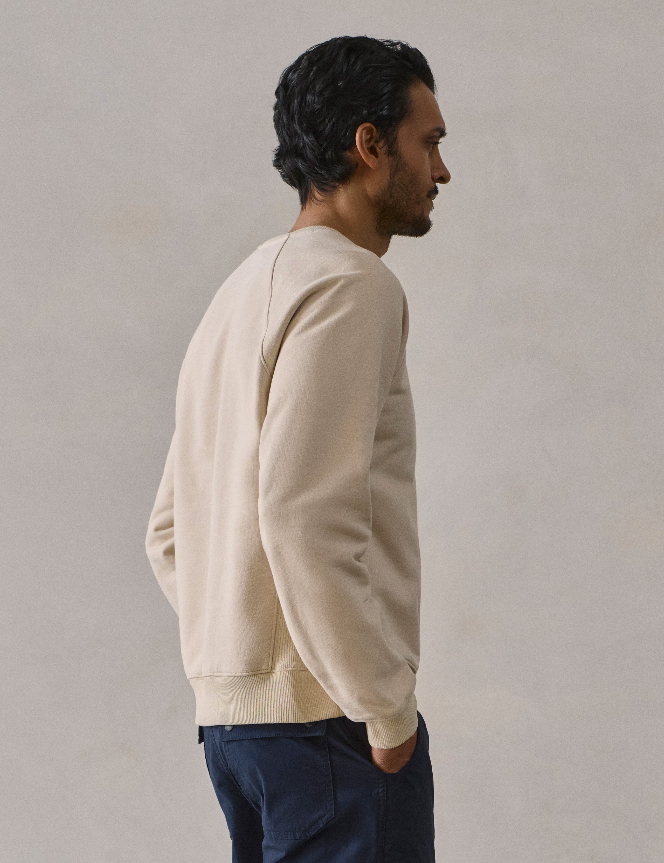 Rear 3/4 upper body view of man wearing Osa Raglan Sweatshirt in Bone white from AETHER Apparel.