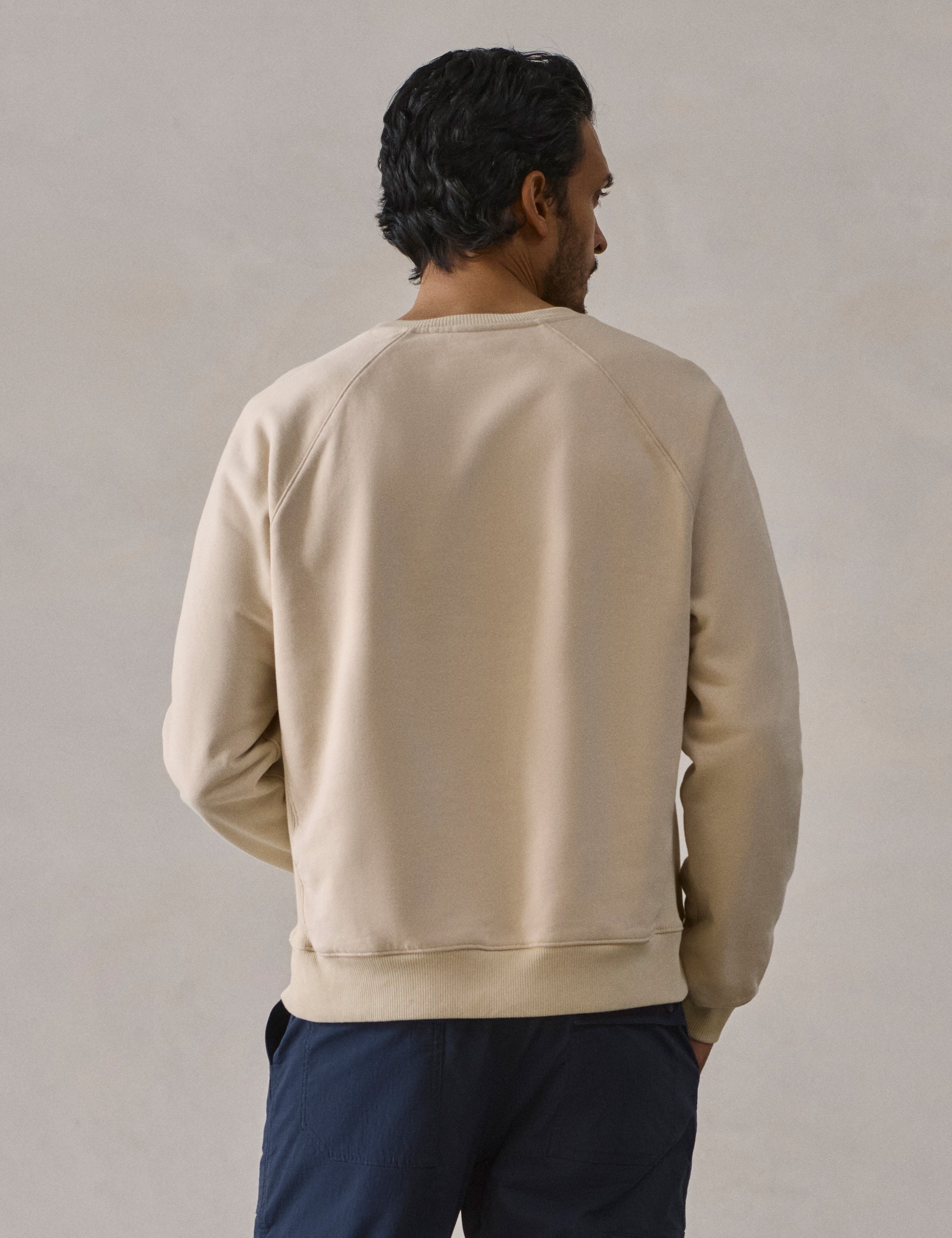 Rear upper body view of man wearing Osa Raglan Sweatshirt in Bone white from AETHER Apparel.
