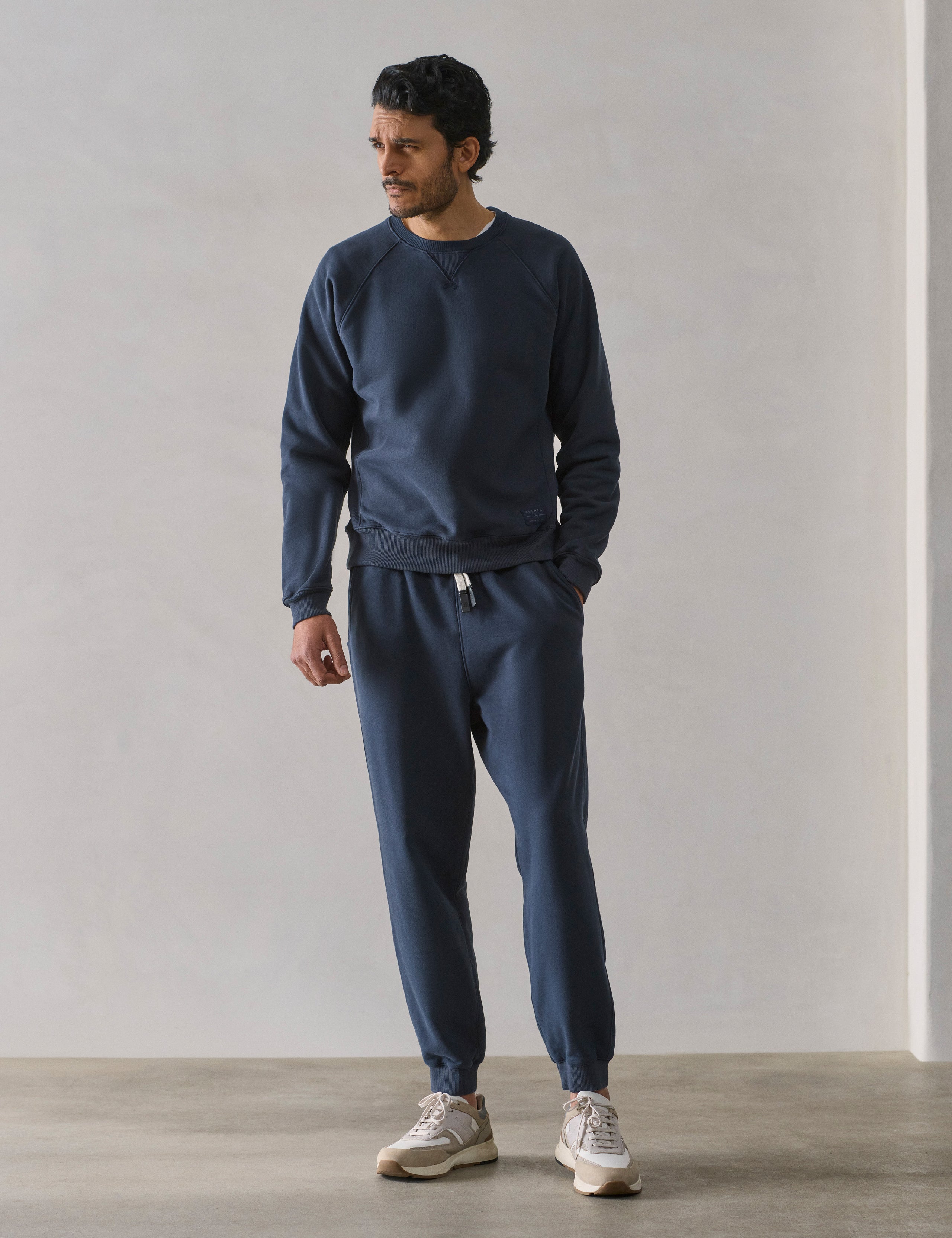 Front full-body view of man wearing Osa Raglan Sweatshirt in Total Eclipse dark blue from AETHER Apparel.