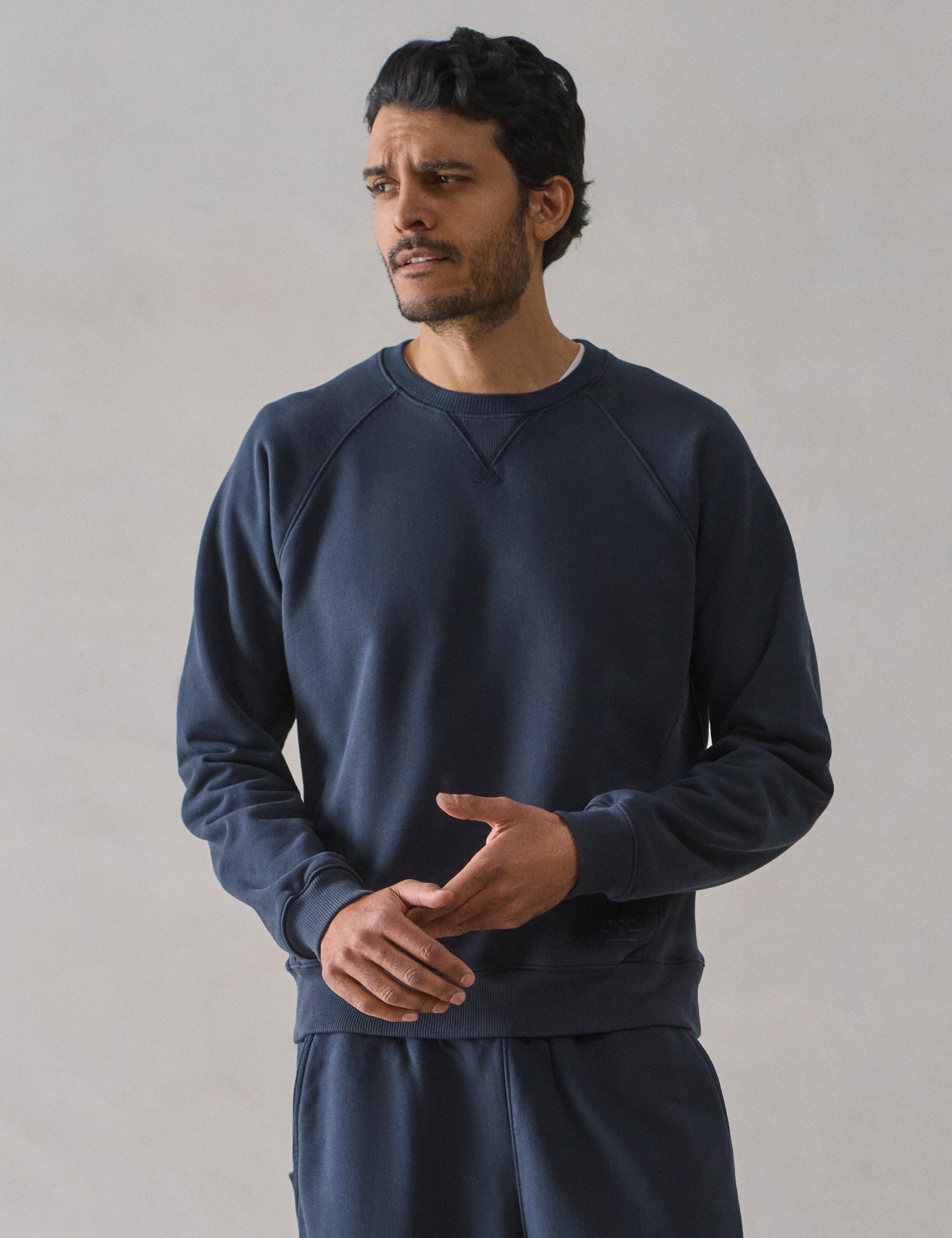 Front upper body view of man wearing Osa Raglan Sweatshirt in Total Eclipse dark blue from AETHER Apparel.