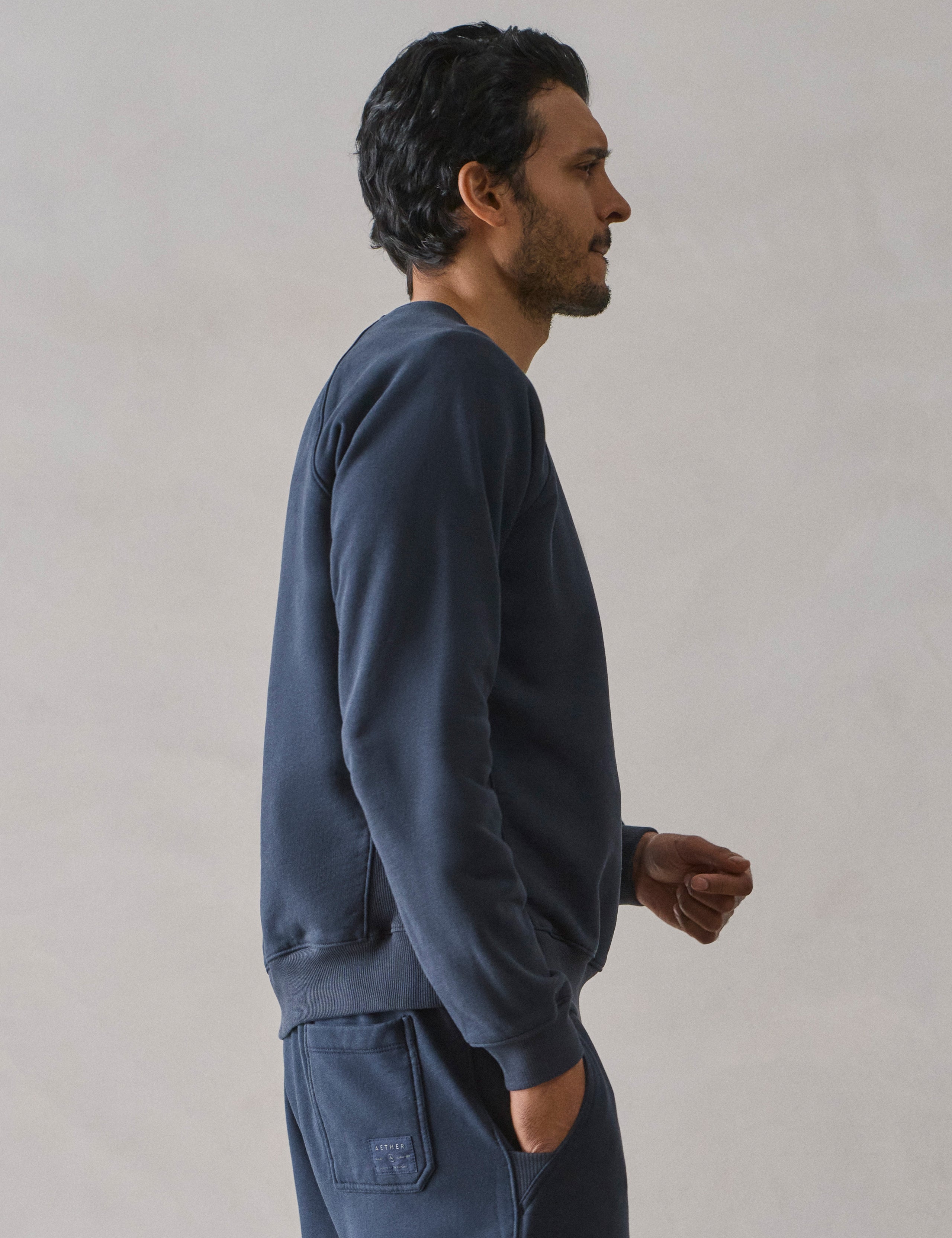 Right side upper body profile view of man wearing Osa Raglan Sweatshirt in Total Eclipse dark blue from AETHER Apparel.