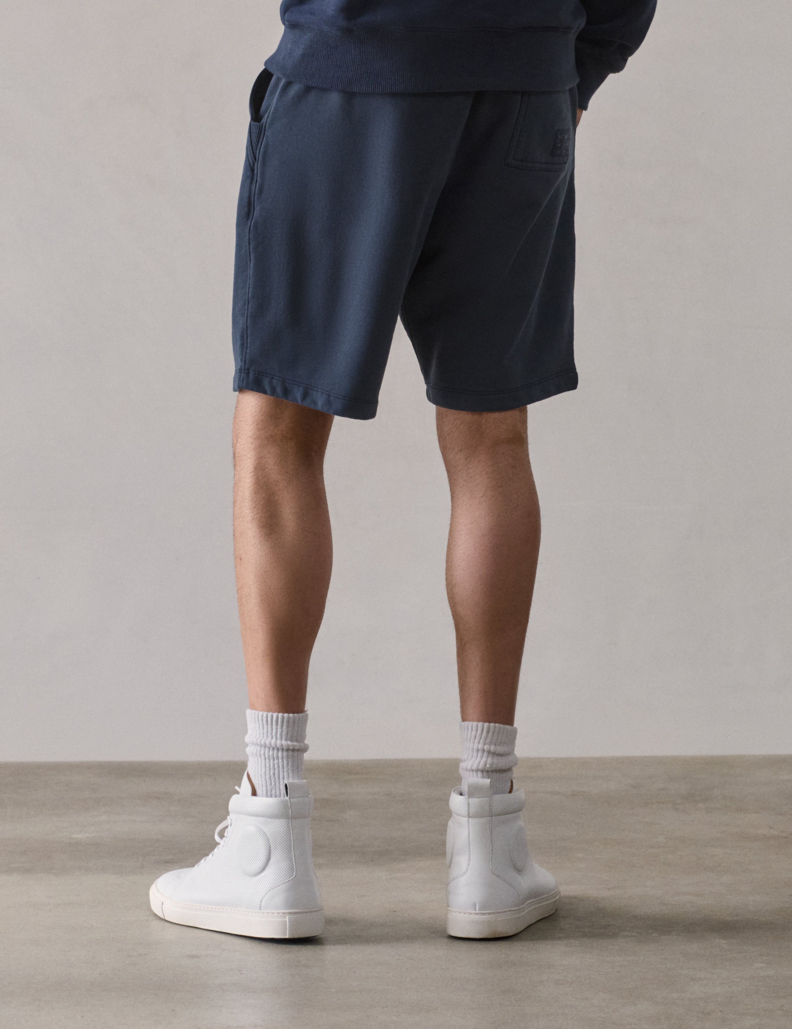 Rear lower body view of man wearing Osa Sweatshort in Total Eclipse dark blue from AETHER Apparel.