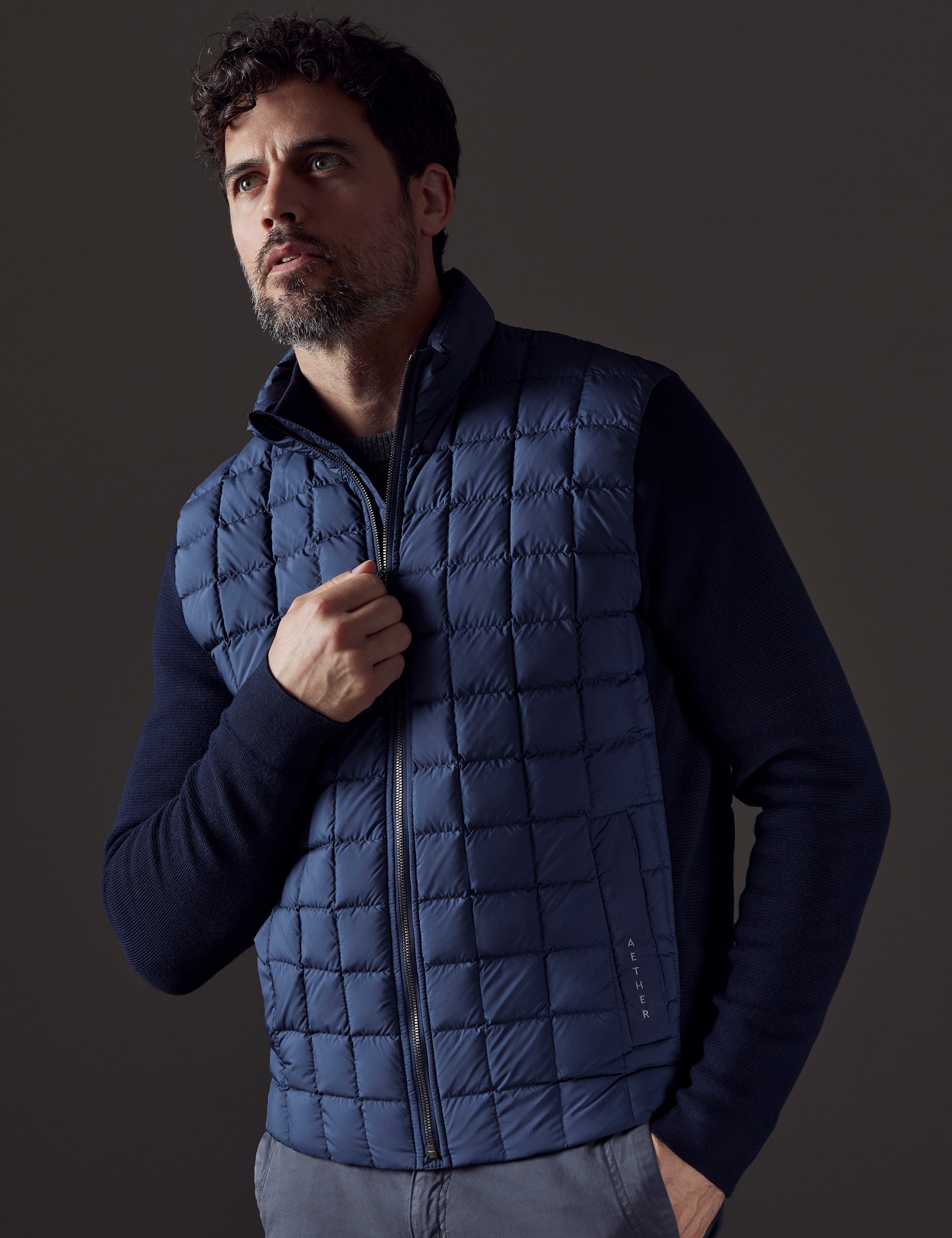 Front 3/4 body view of man with hand on zipper of Phase Full-Zip in Total Eclipse dark blue from AETHER Apparel.