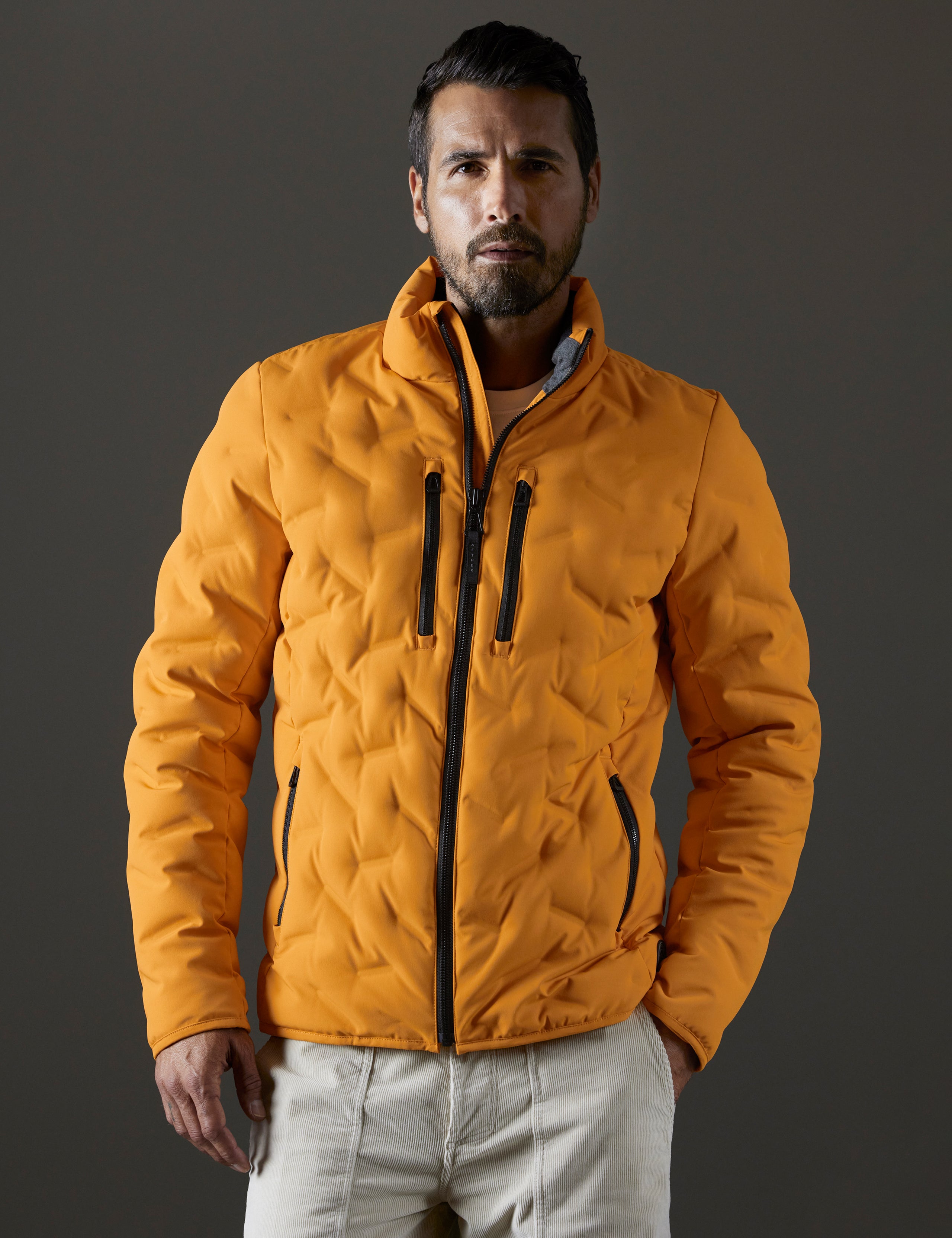 Front body view of man wearing Rex Down Jacket in Midas Orange from AETHER Apparel.