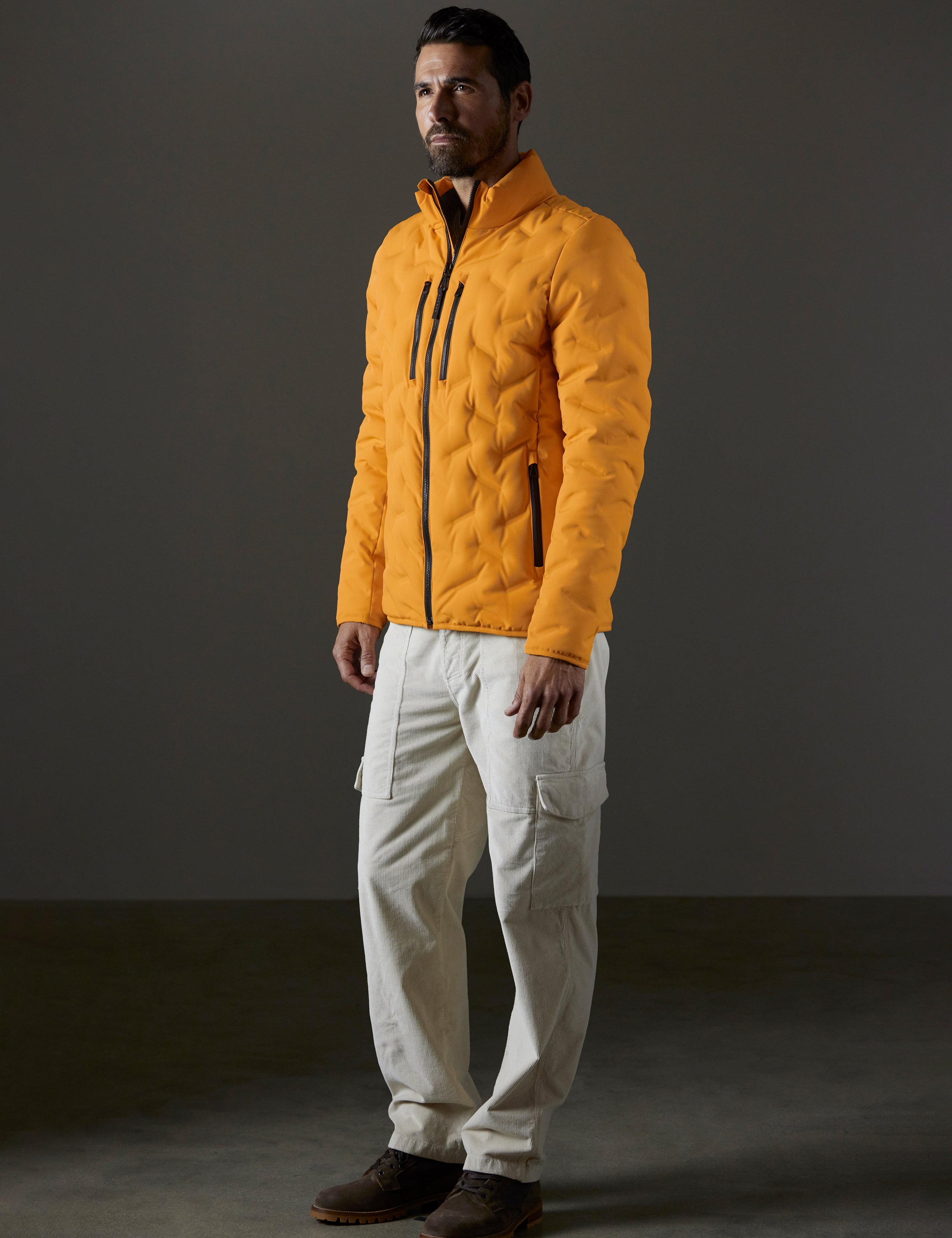 Front 3/4 full-body view of man wearing Rex Down Jacket in Midas Orange from AETHER Apparel.