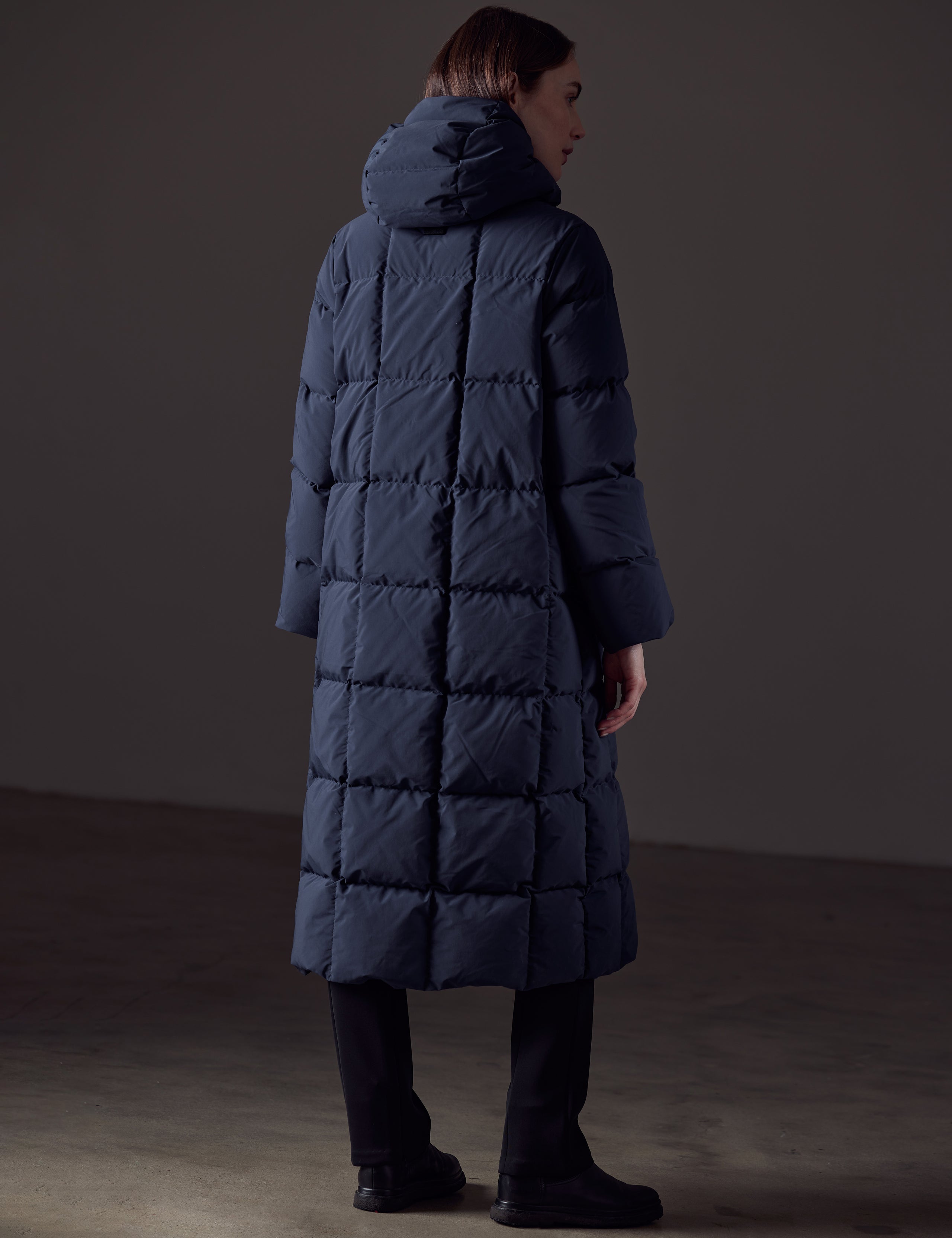 Rear angled full-body view of woman wearing Shaw Jacket in Nordic Navy Blue from AETHER Apparel.
