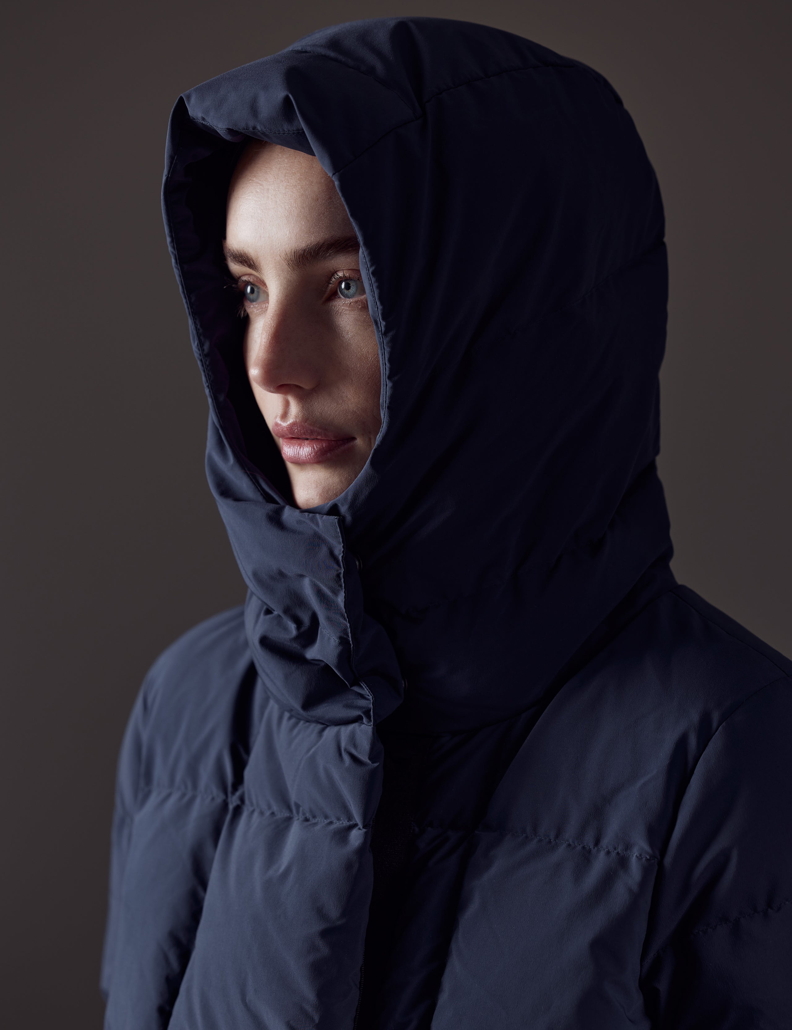 Closeup front angled view of woman with hood up wearing Shaw Jacket in Nordic Navy Blue from AETHER Apparel.