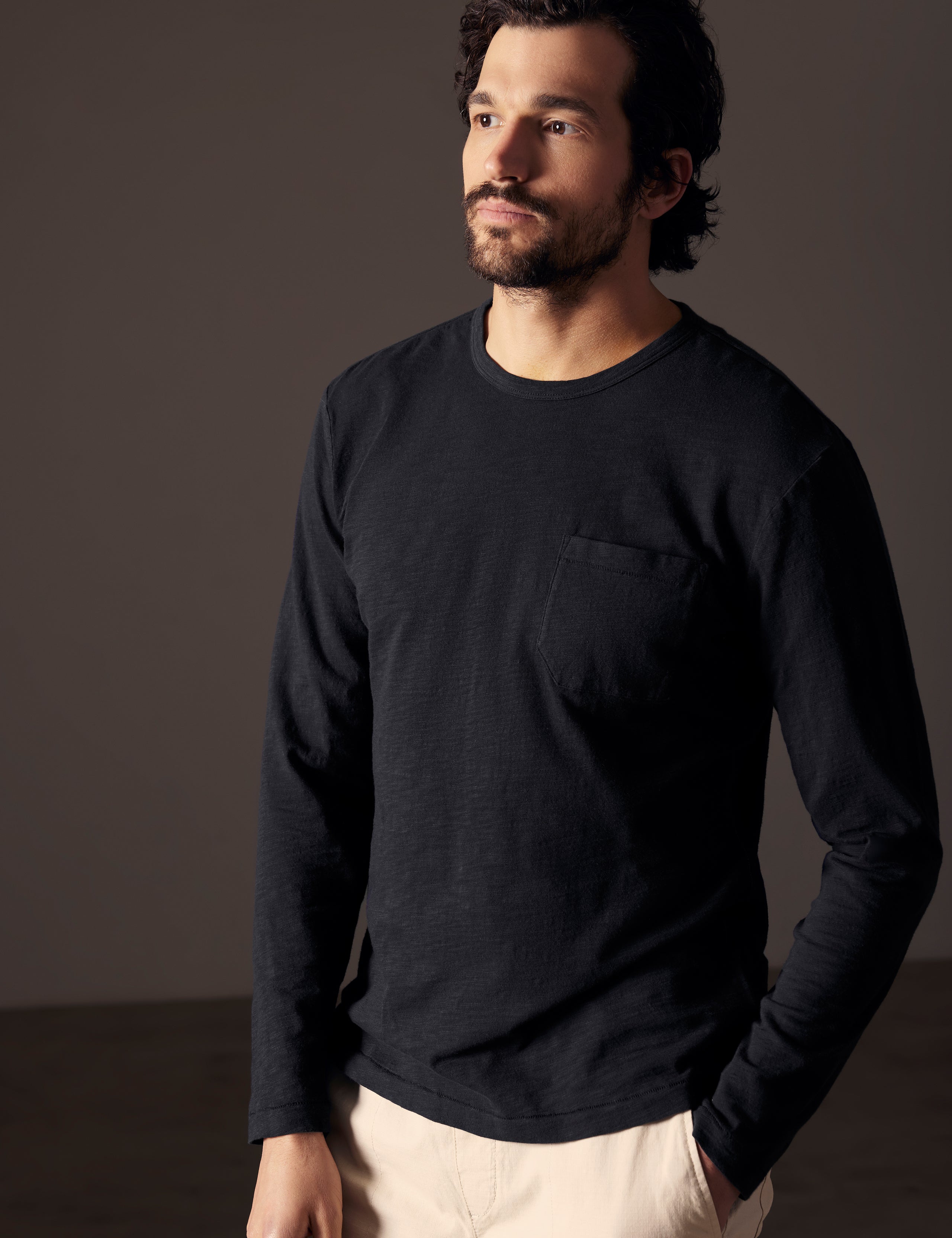 Front angled body view of man with hand in pant pocket wearing Slub Long-Sleeve Tee in Onyx Black from AETHER Apparel.