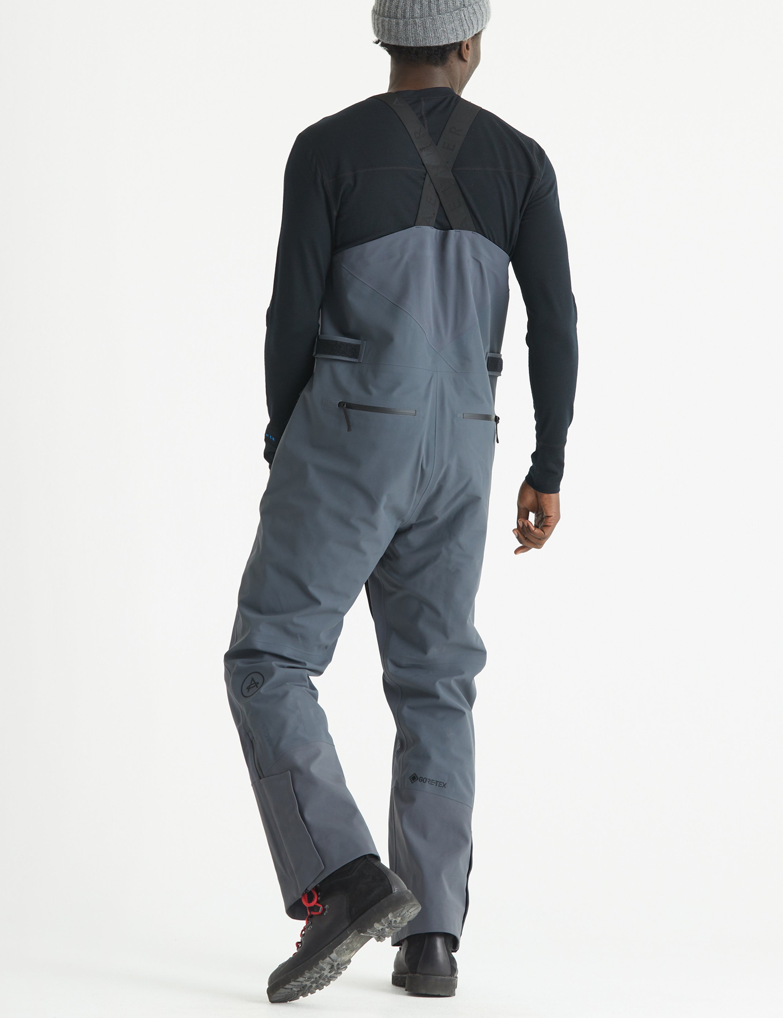 Rear angled full-body view of man wearing Stealth Snow Bib in Graphite from AETHER Apparel.