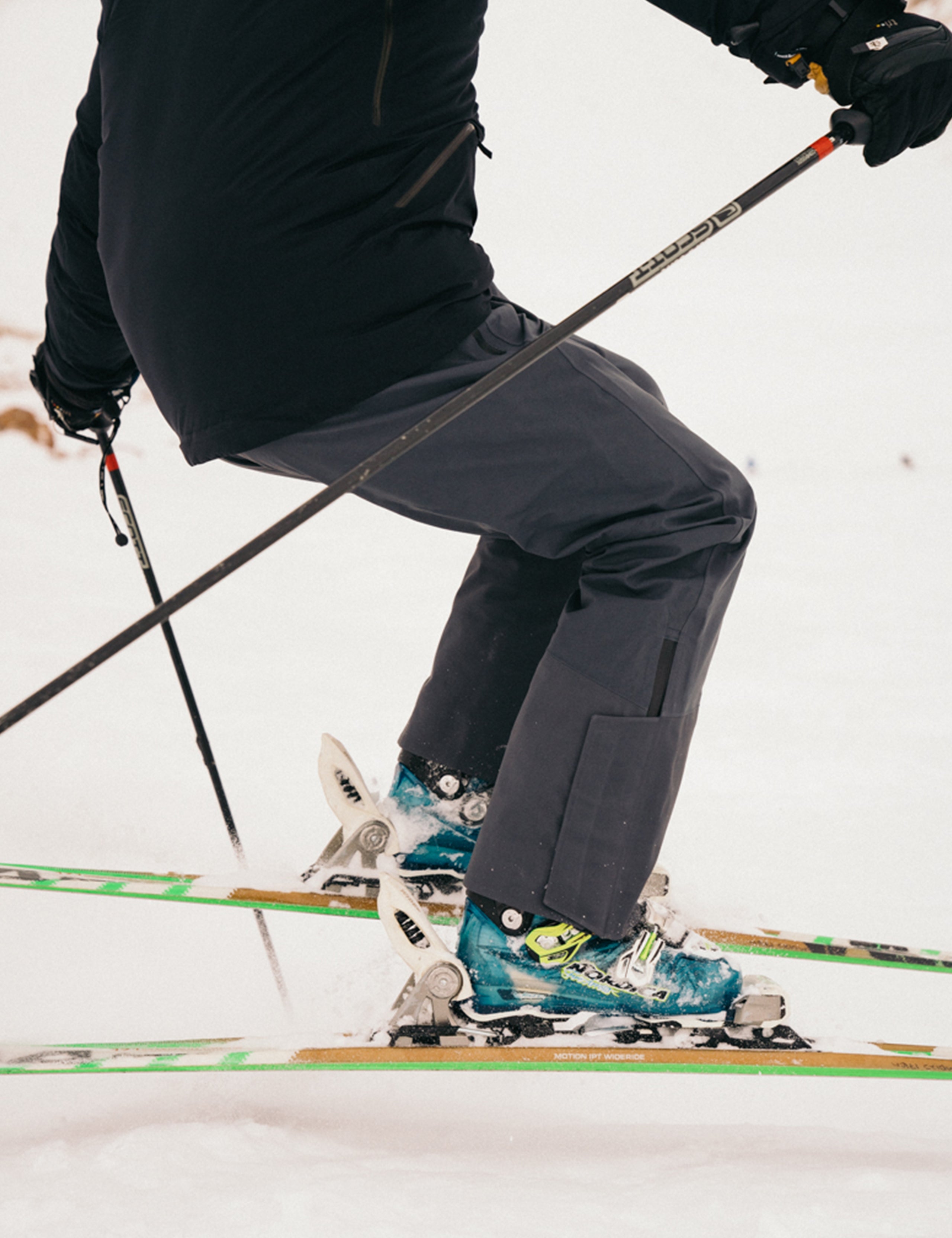 Outdoor lifestyle image of lower body of man riding skis wearing Stealth Snow Bib in Graphite from AETHER Apparel.