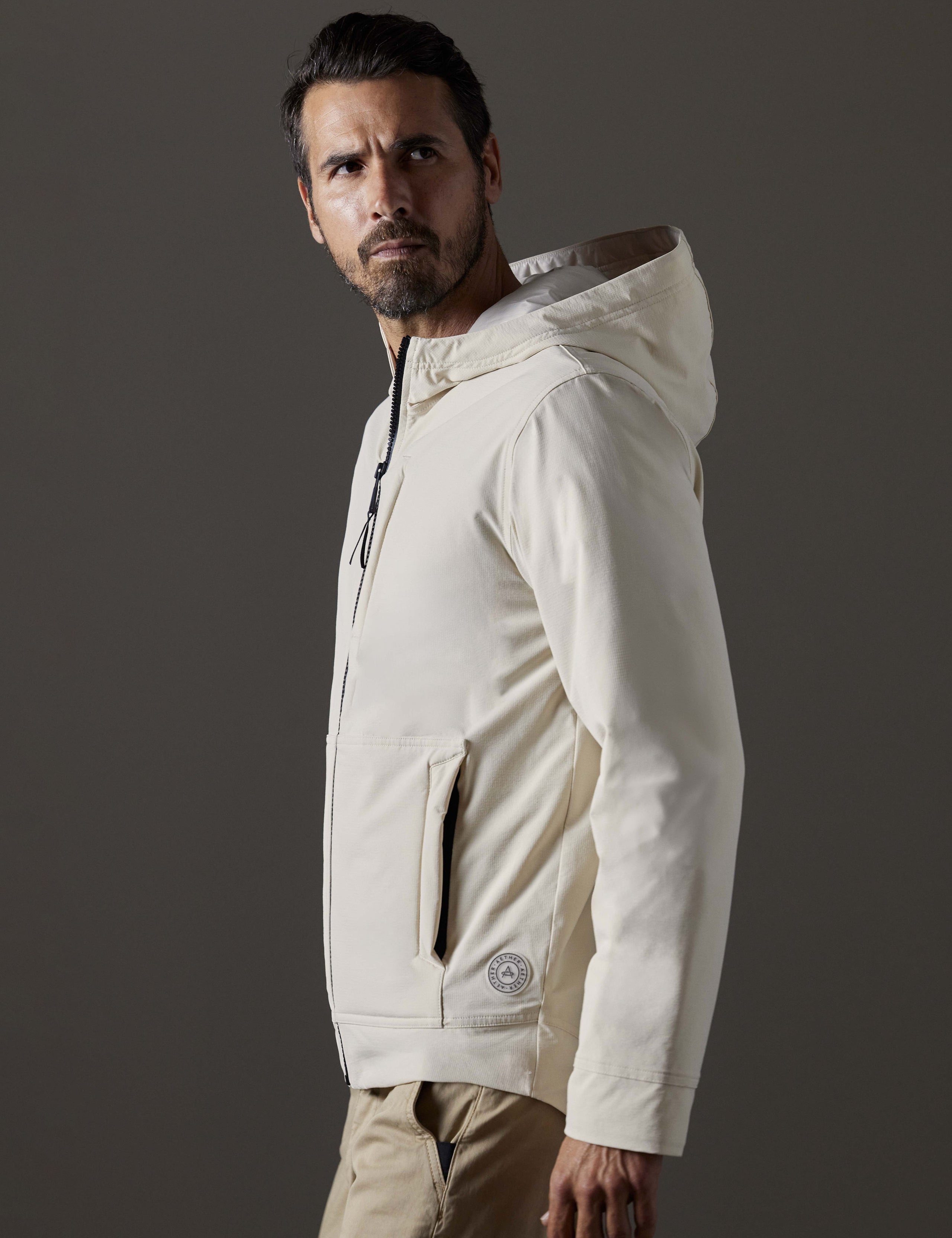 Side profile body view of man wearing Stornaway Insulated Hoodie in Bone white from AETHER Apparel.