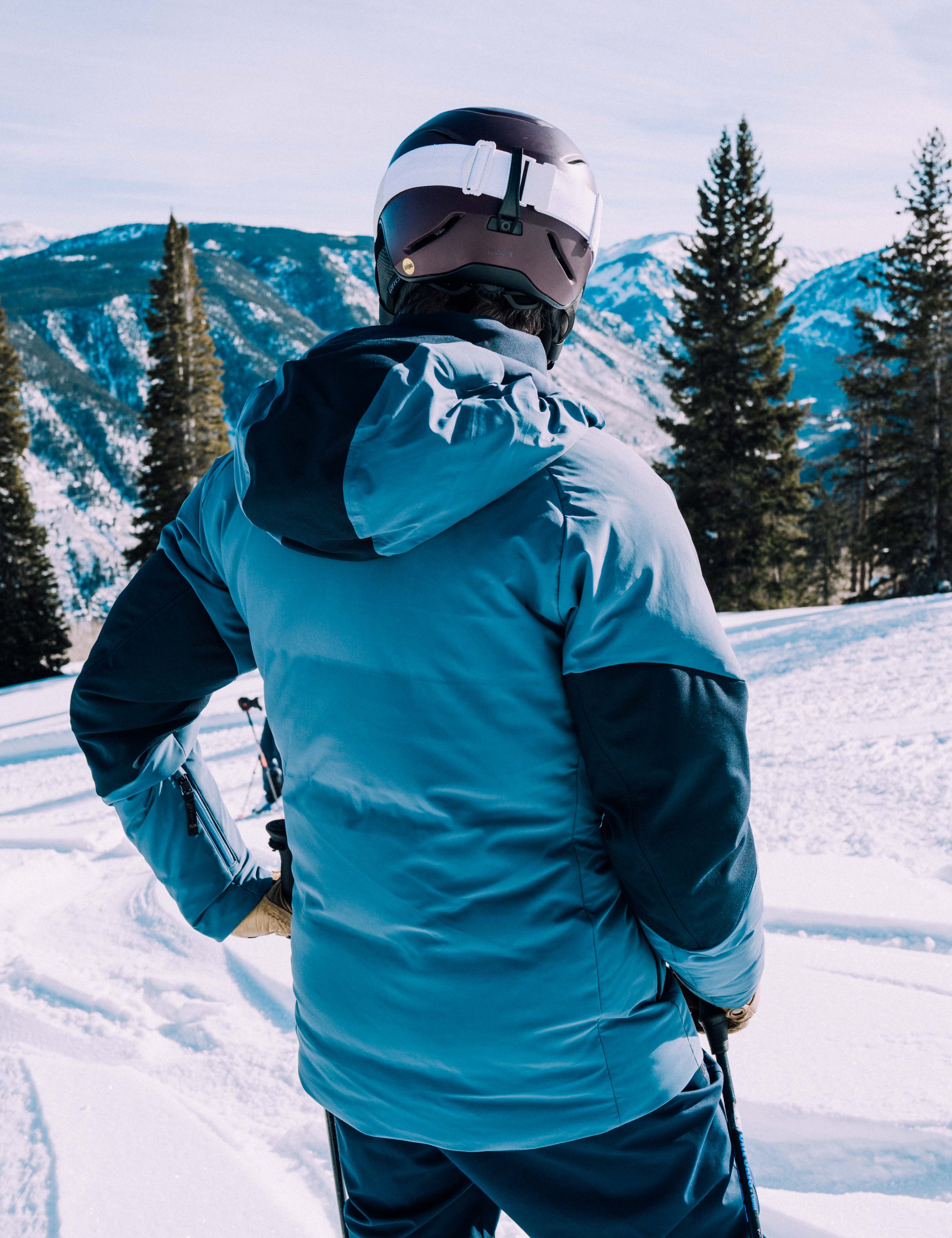 Outdoor lifestyle image of back of man on snowcovered hill wearing Torino Jacket in Baltic Blue from AETHER Apparel.