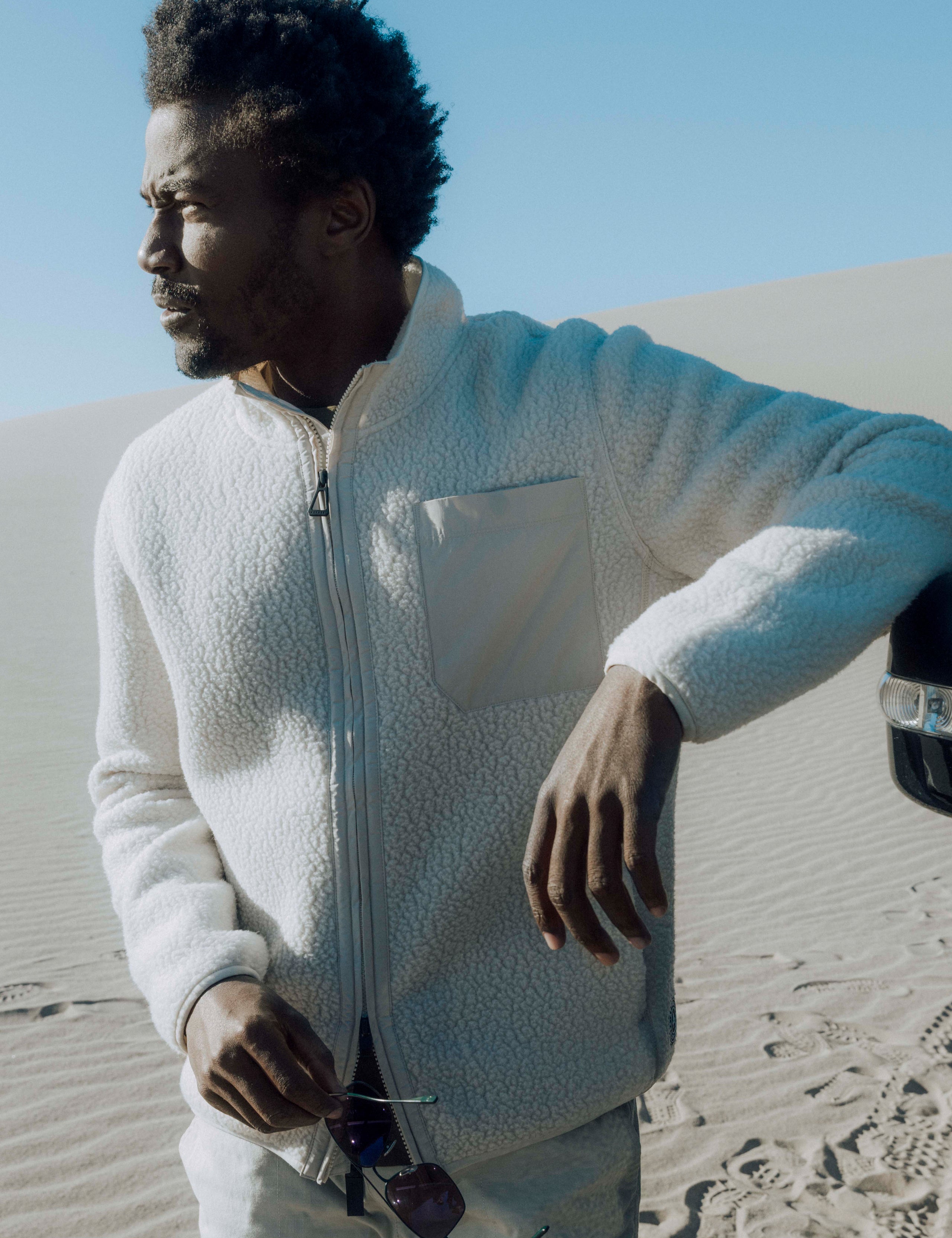 Outdoor lifestyle shot of man standing next to lake wearing Walsh Full-Zip in Bone white from AETHER Apparel.