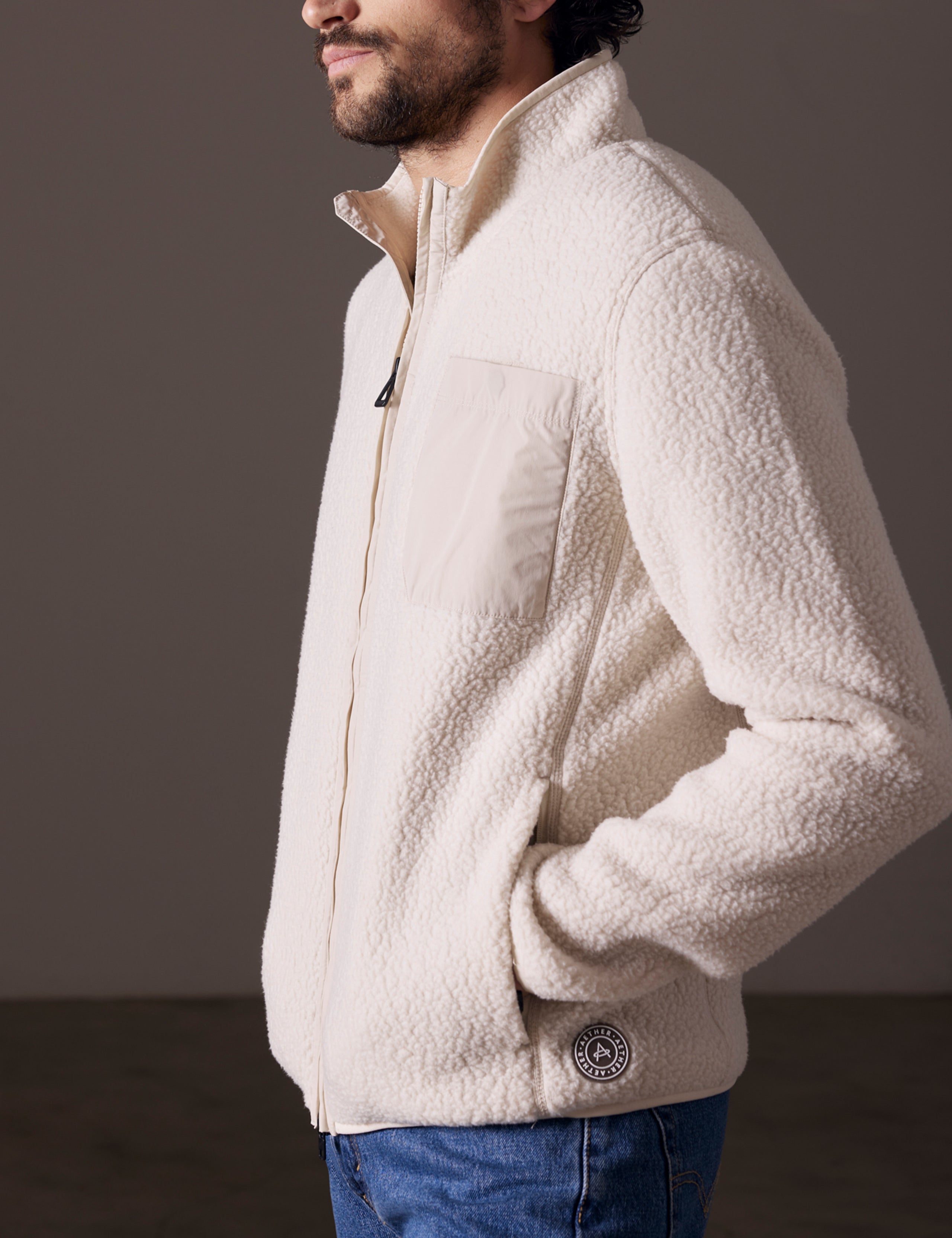 Side profile body view of man wearing Walsh Full-Zip in Bone white from AETHER Apparel.