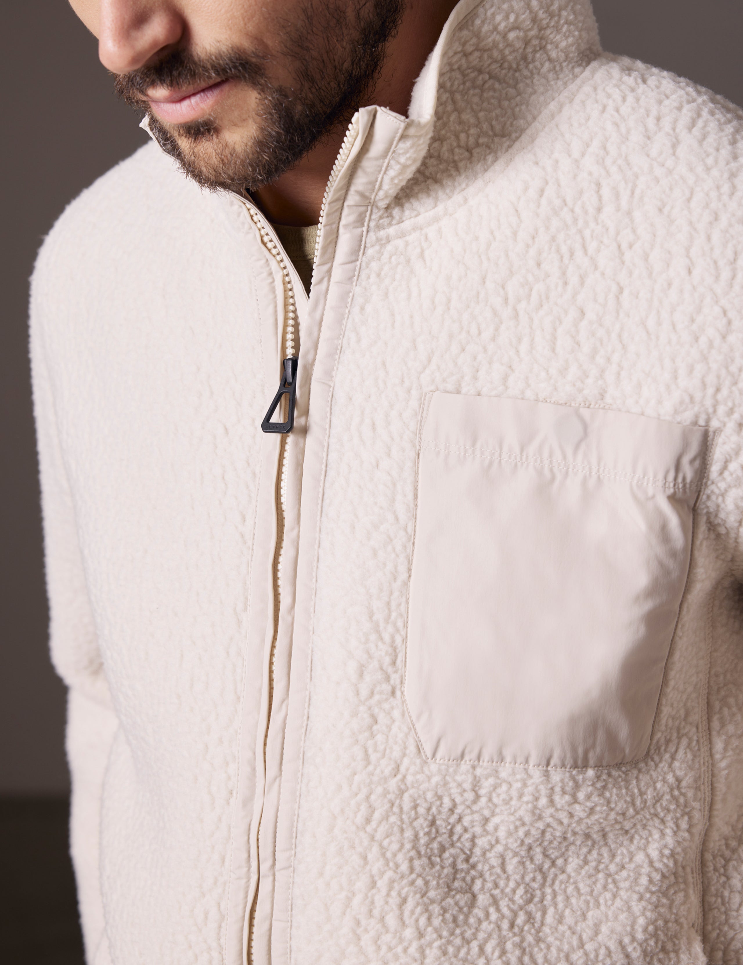 Closeup view of main zipper, chest pocket, and fabric of Walsh Full-Zip in Bone white from AETHER Apparel.