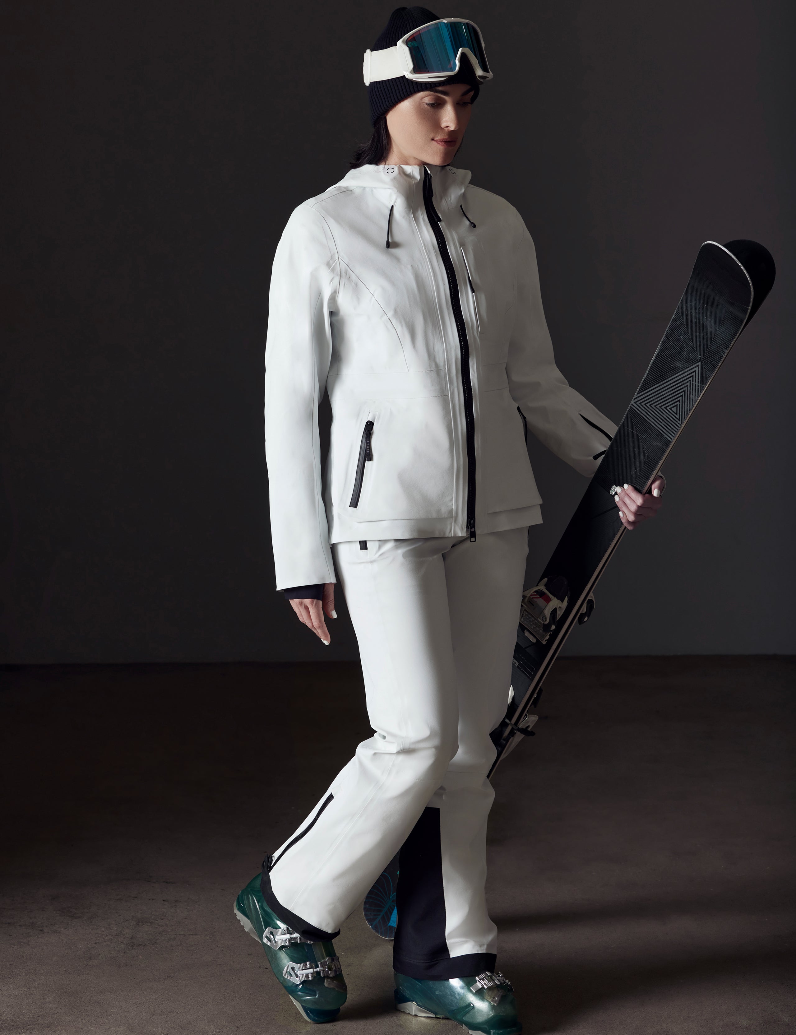 Front angled full-body view of woman holding skis wearing Boyd Snow Jacket in White from AETHER Apparel.
