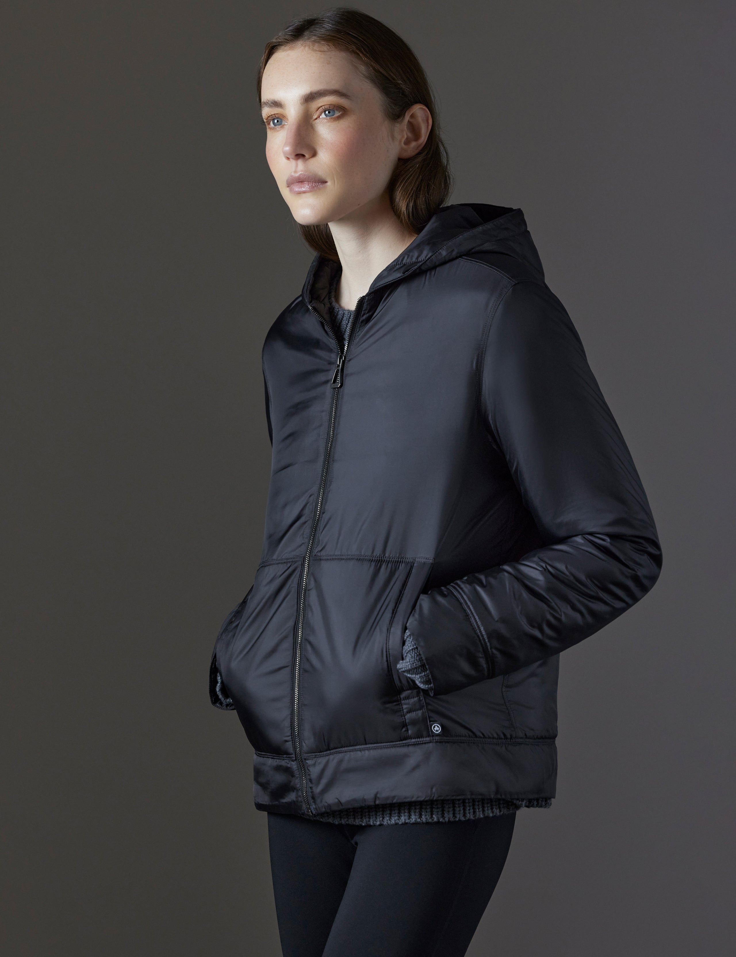 Front angled view of woman with hands in pockets wearing Eco Space Hoodie in Onyx Black from AETHER Apparel.
