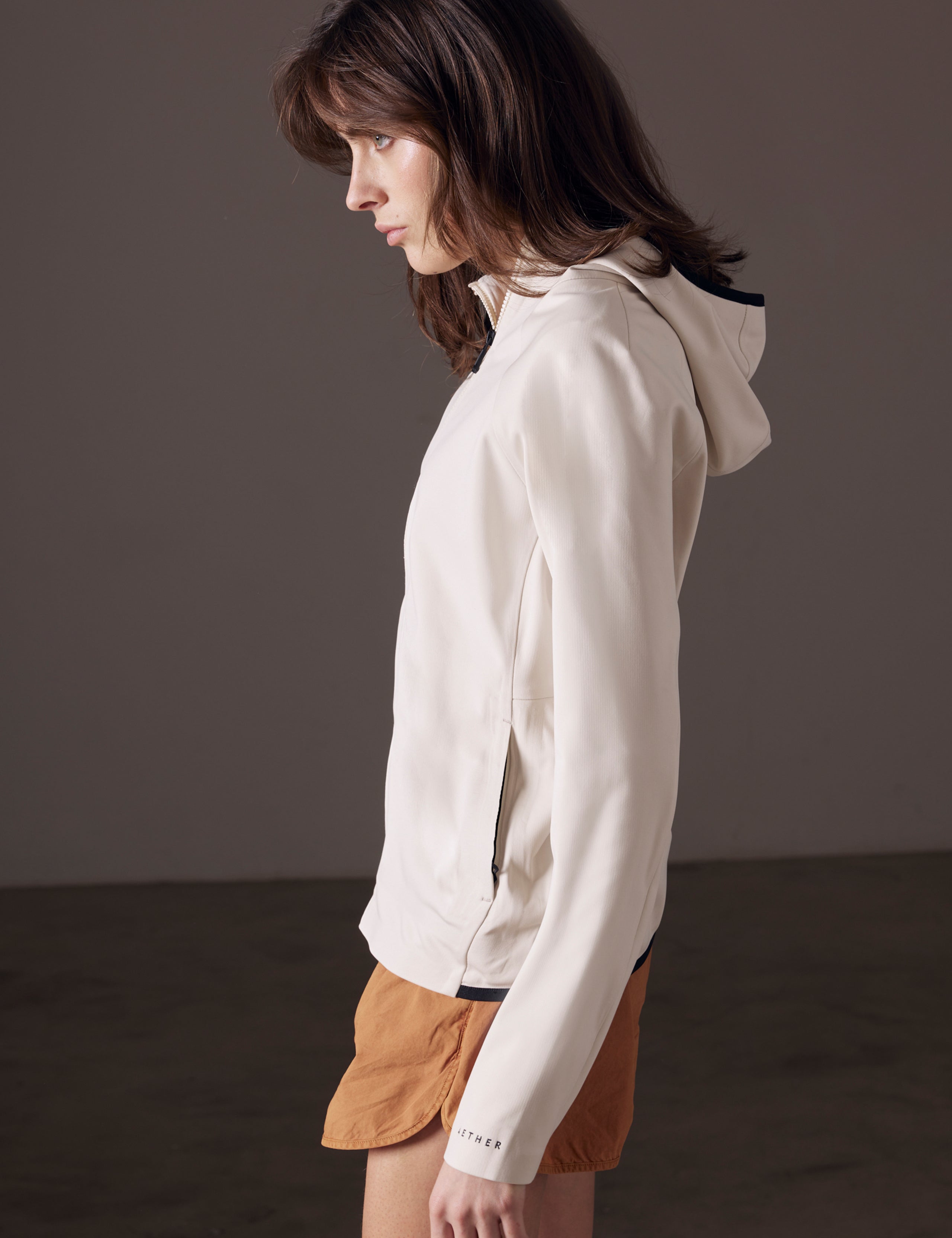 Side profile view of woman wearing Hooded Tech-Fleece Full-Zip in Bone white from AETHER Apparel.