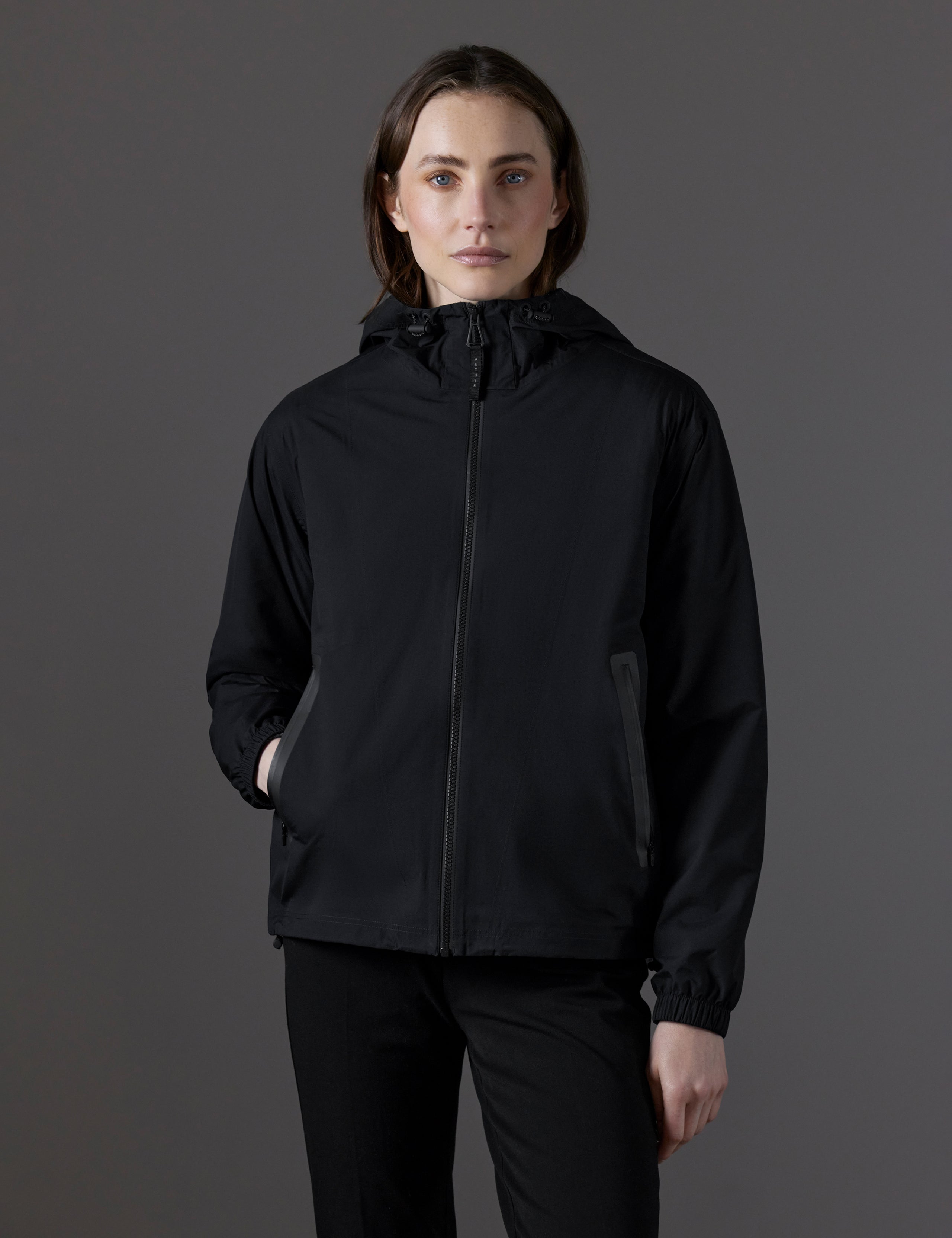 Front body view of woman with hand in pocket wearing Kite Lightweight Jacket in Onyx Black from AETHER Apparel.
