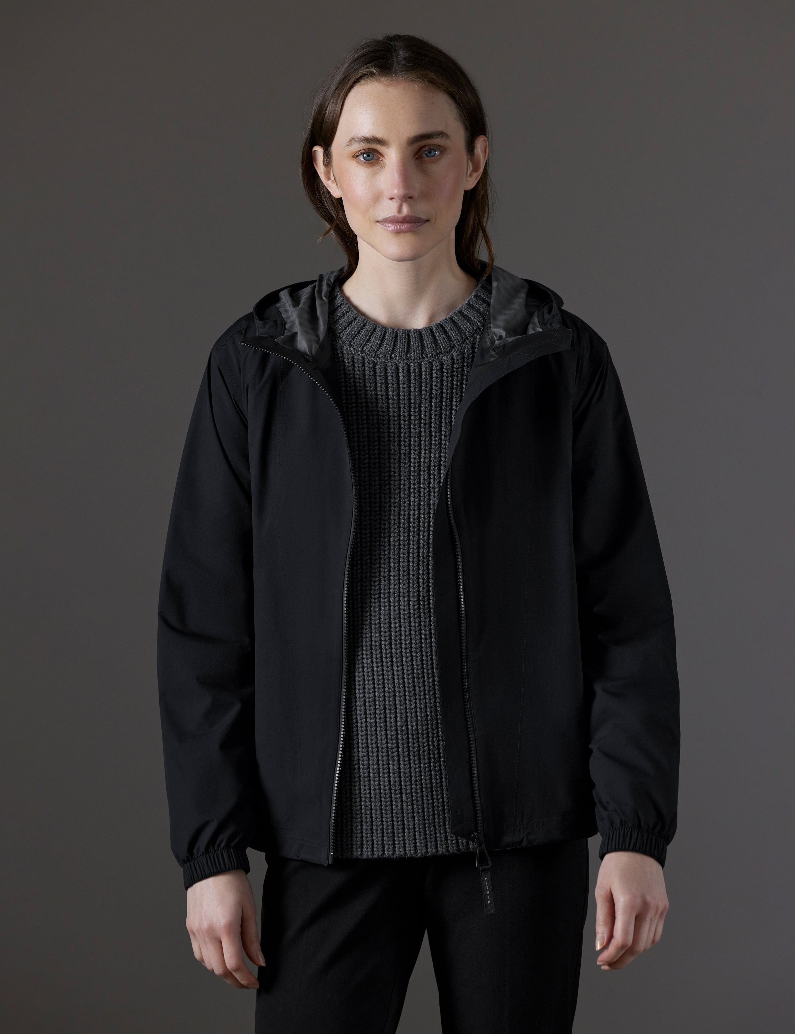 Front body view of woman wearing unzipped Kite Lightweight Jacket in Onyx Black from AETHER Apparel.
