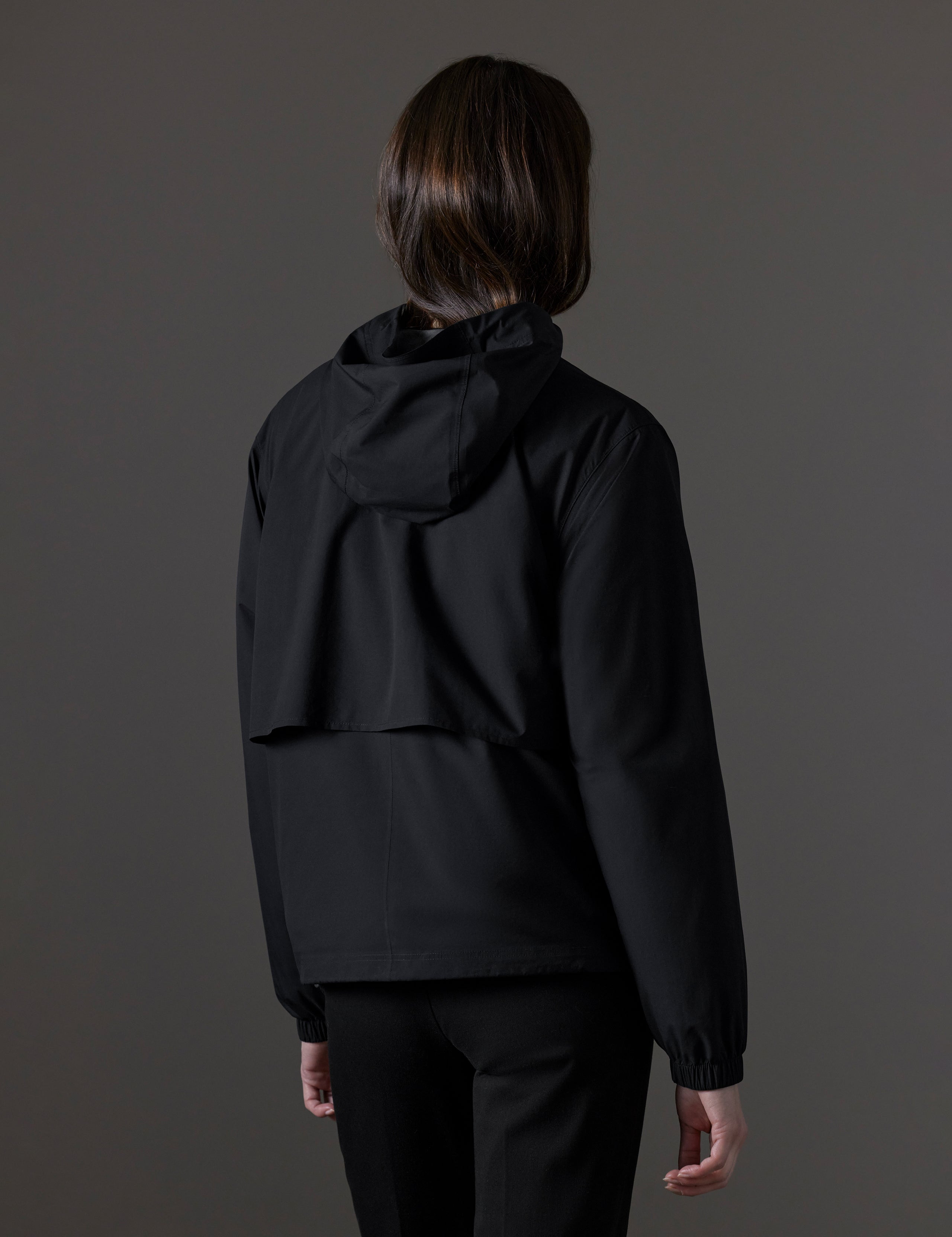 Rear angled view of woman wearing Kite Lightweight Jacket in Onyx Black from AETHER Apparel.