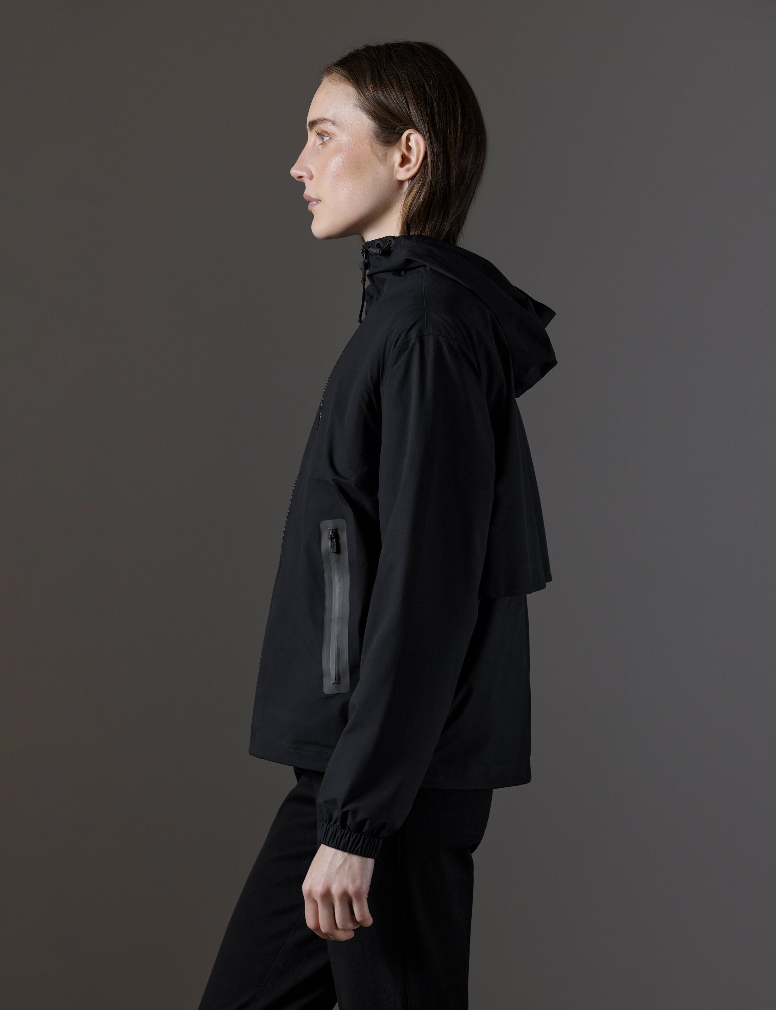 Side profile view of woman wearing Kite Lightweight Jacket in Onyx Black from AETHER Apparel.