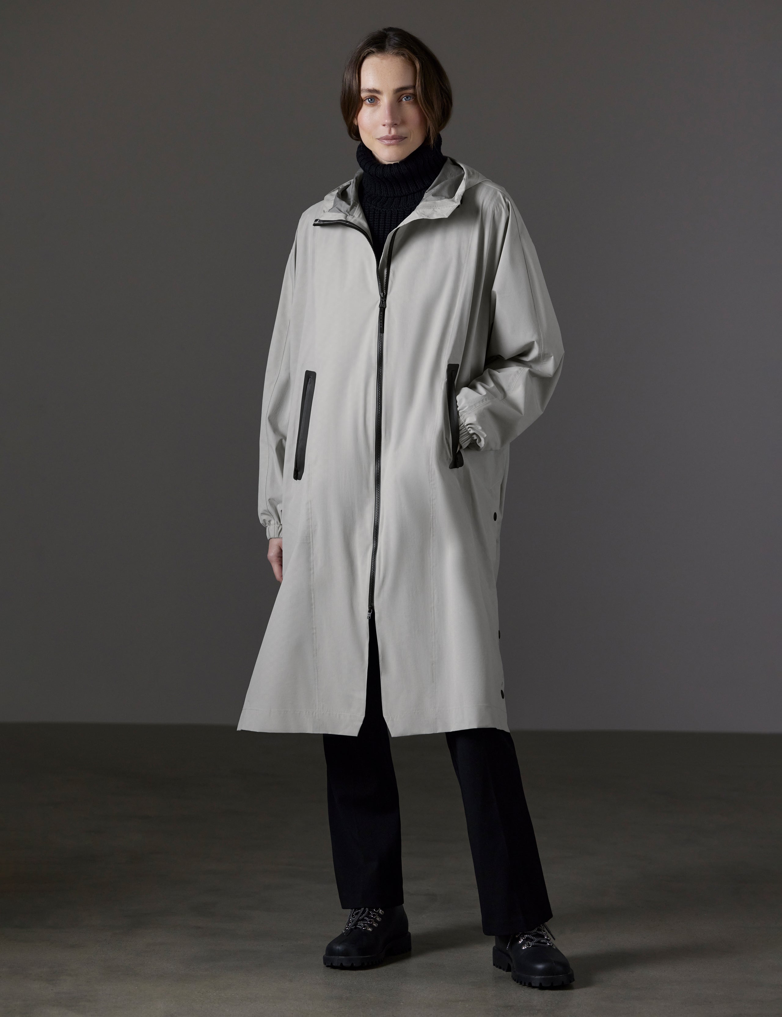 Front angled full-body view of woman wearing Kite Packable Rain Poncho in Stone Grey from AETHER Apparel.