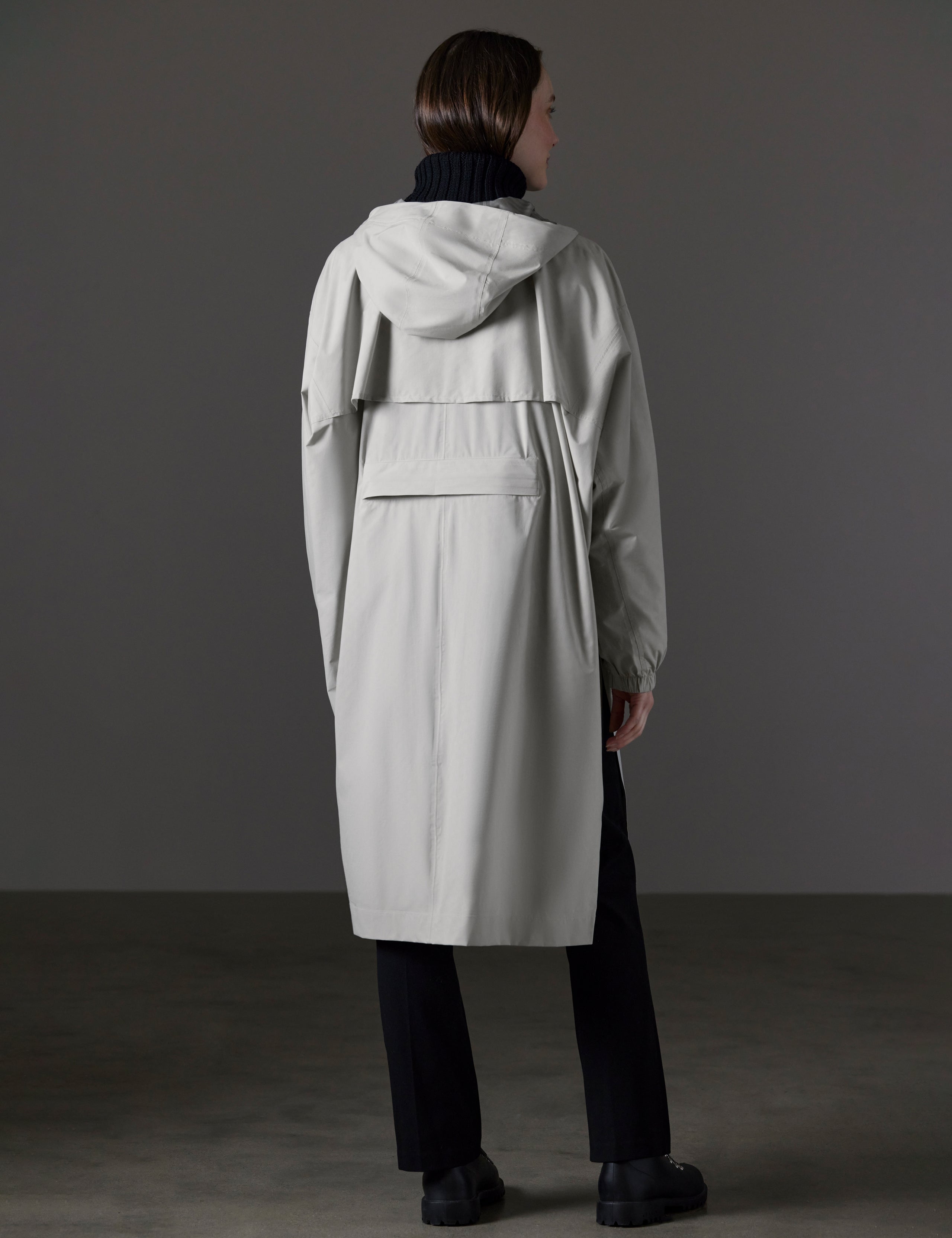 Rear angled full-body view of woman wearing Kite Packable Rain Poncho in Stone Grey from AETHER Apparel.