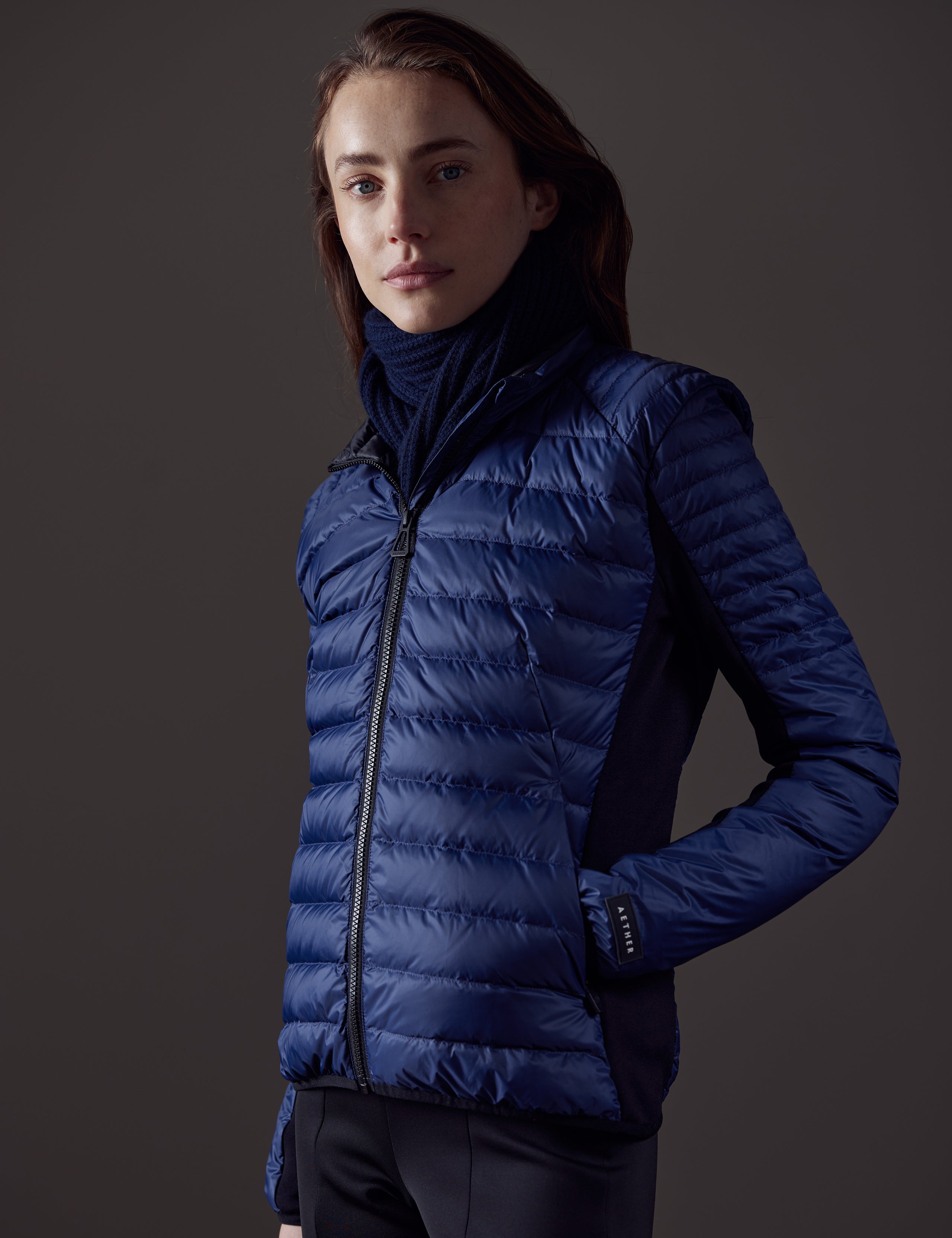 Front angled view of woman with hand in coat pocket wearing Ozone Jacket in Nordic Navy blue from AETHER Apparel.