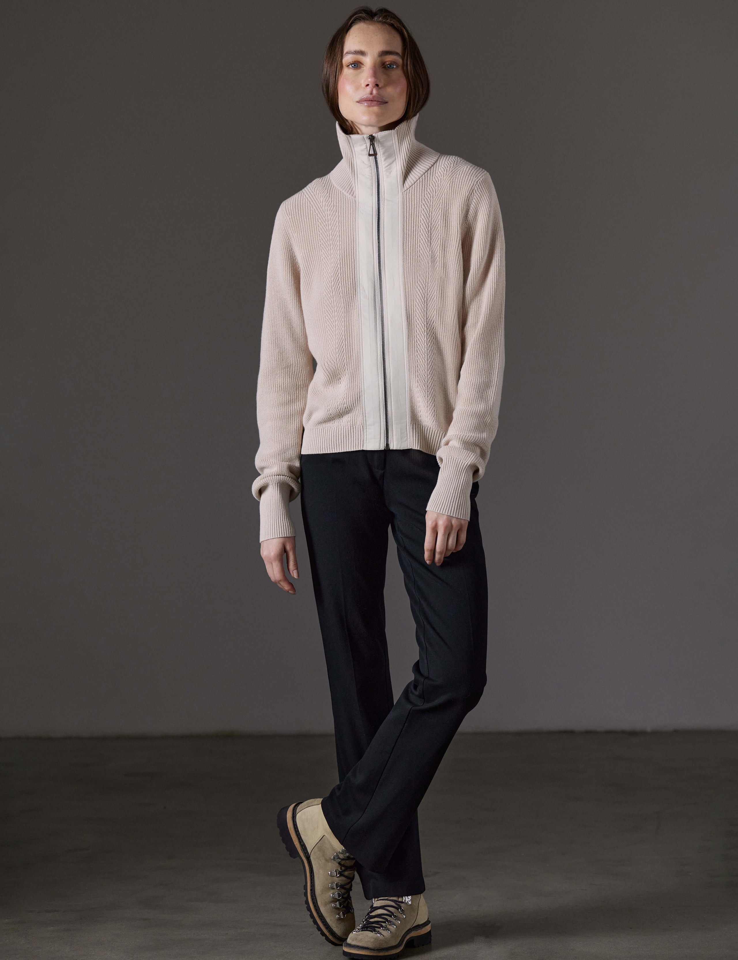 Front full-body view of woman standing with legs crossed wearing Rhea Full-Zip Sweater in Bone white from AETHER Apparel.