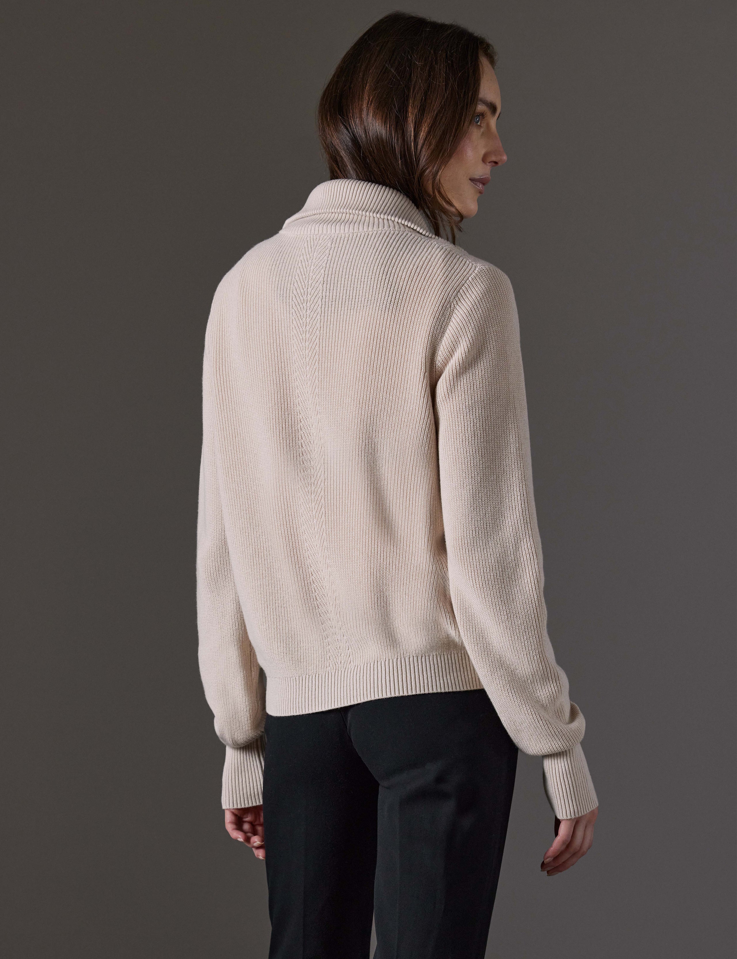 Rear angled view of woman wearing Rhea Full-Zip Sweater in Bone white from AETHER Apparel.