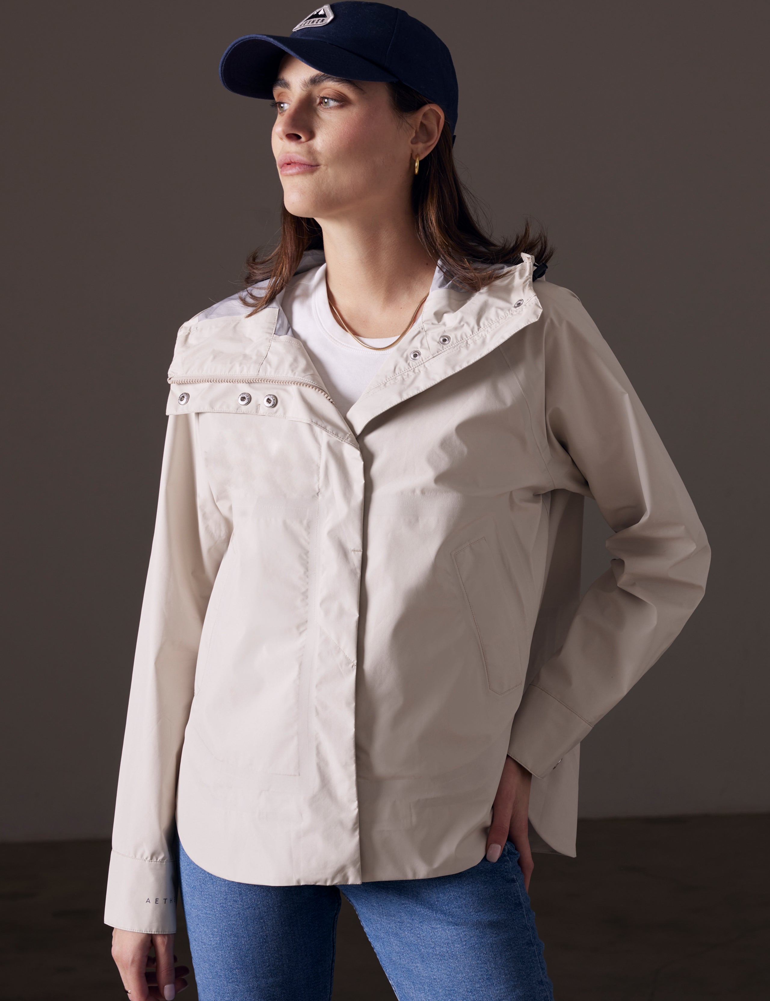 Front angled view of woman with hand on hip wearing Storm All-Weather Jacket in Bone white from AETHER Apparel.