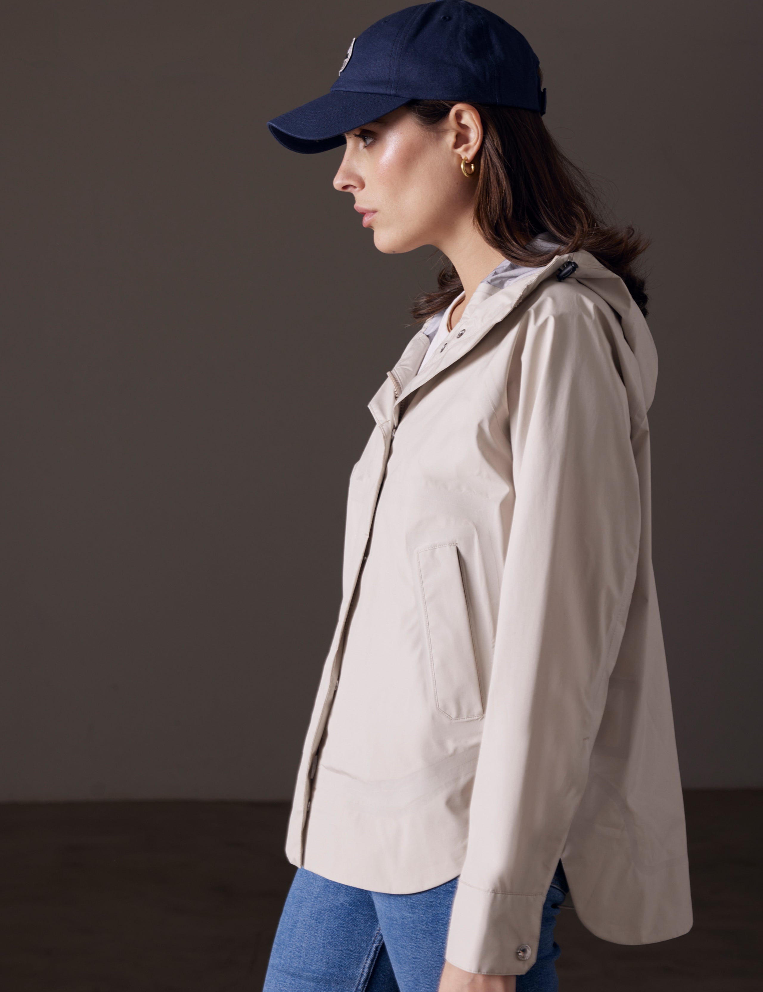 Side profile body view of woman wearing Storm All-Weather Jacket in Bone white from AETHER Apparel.