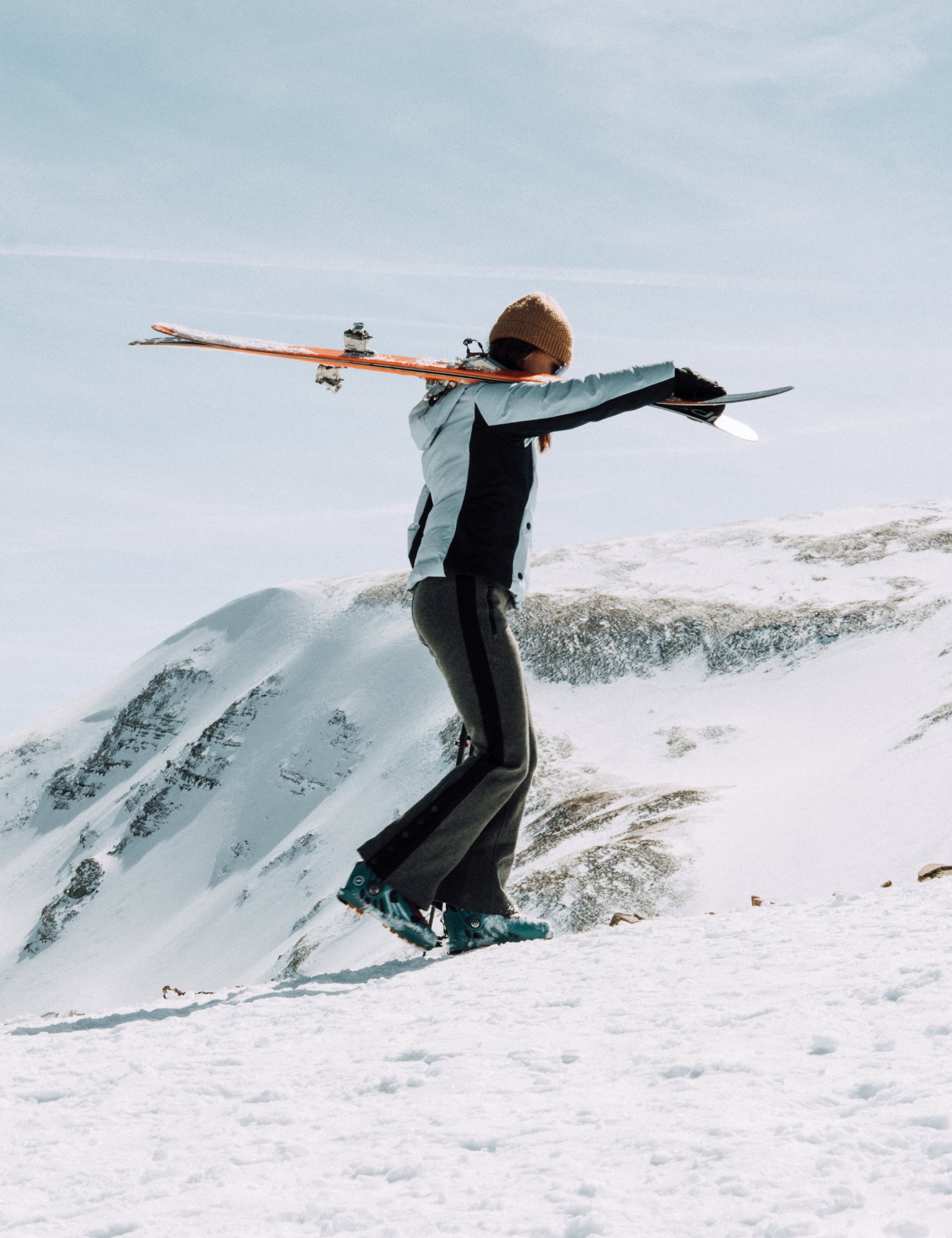 Outdoor lifestyle image of woman carrying skis over shoulder wearing Torino Jacket in Vista Blue from AETHER Apparel.