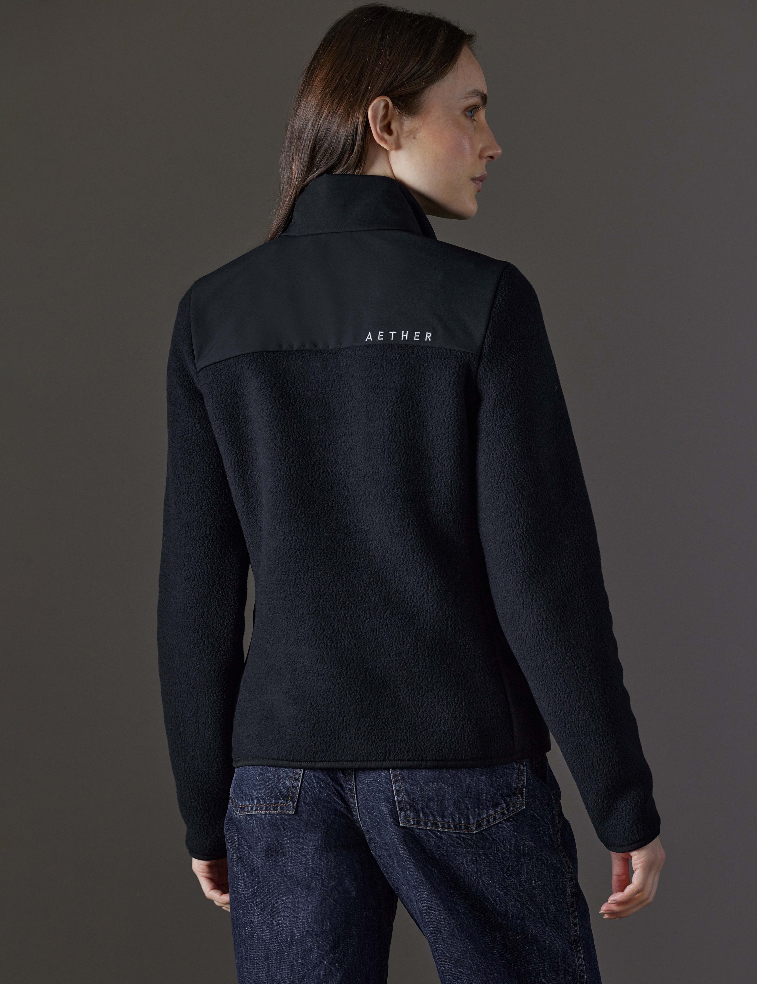 Rear angled body view of woman wearing Walsh Full-Zip 2.0 in Onyx Black from AETHER Apparel.
