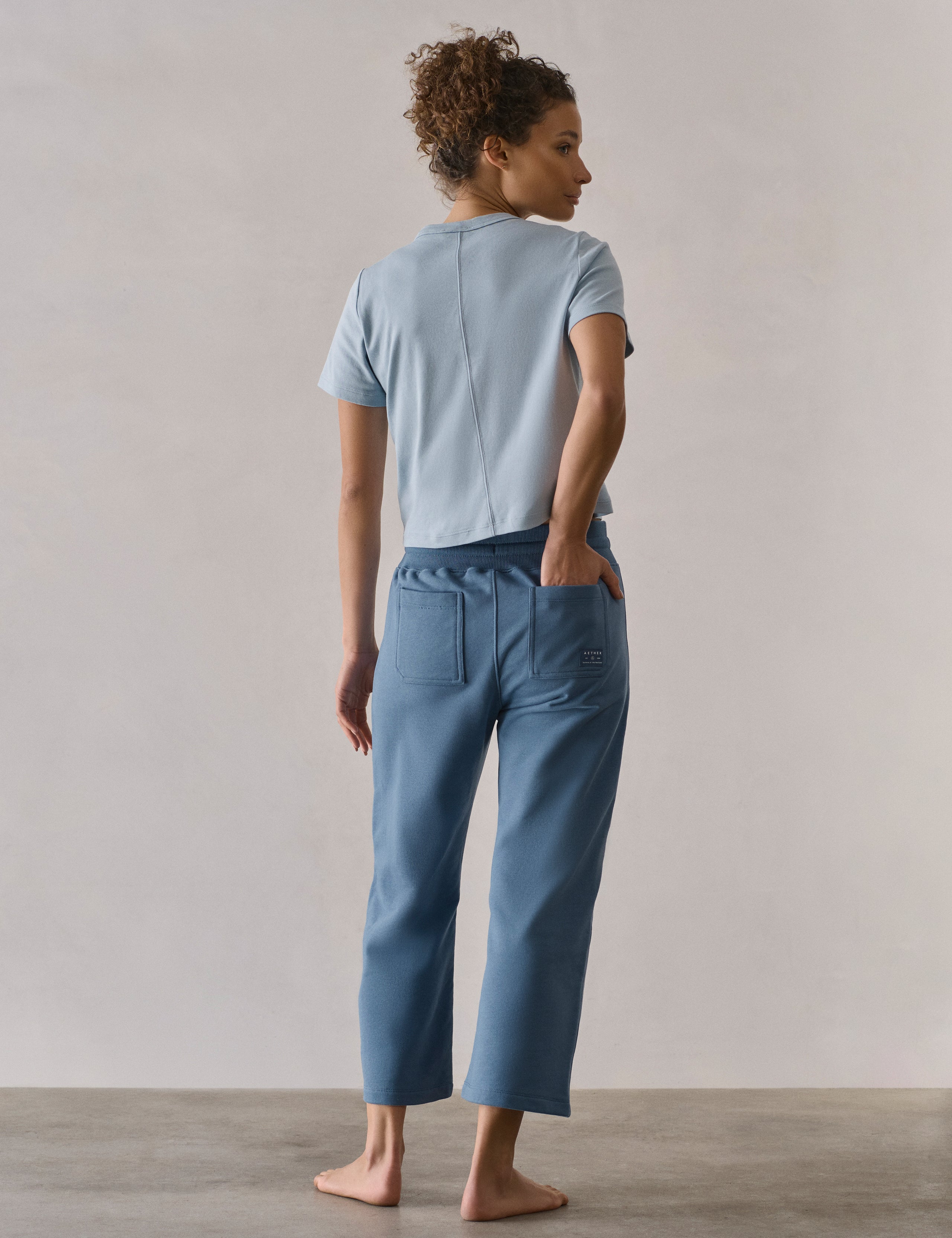 Rear full-body view of woman wearing W Osa Cropped Sweatpant in Coastal Blue from AETHER Apparel.