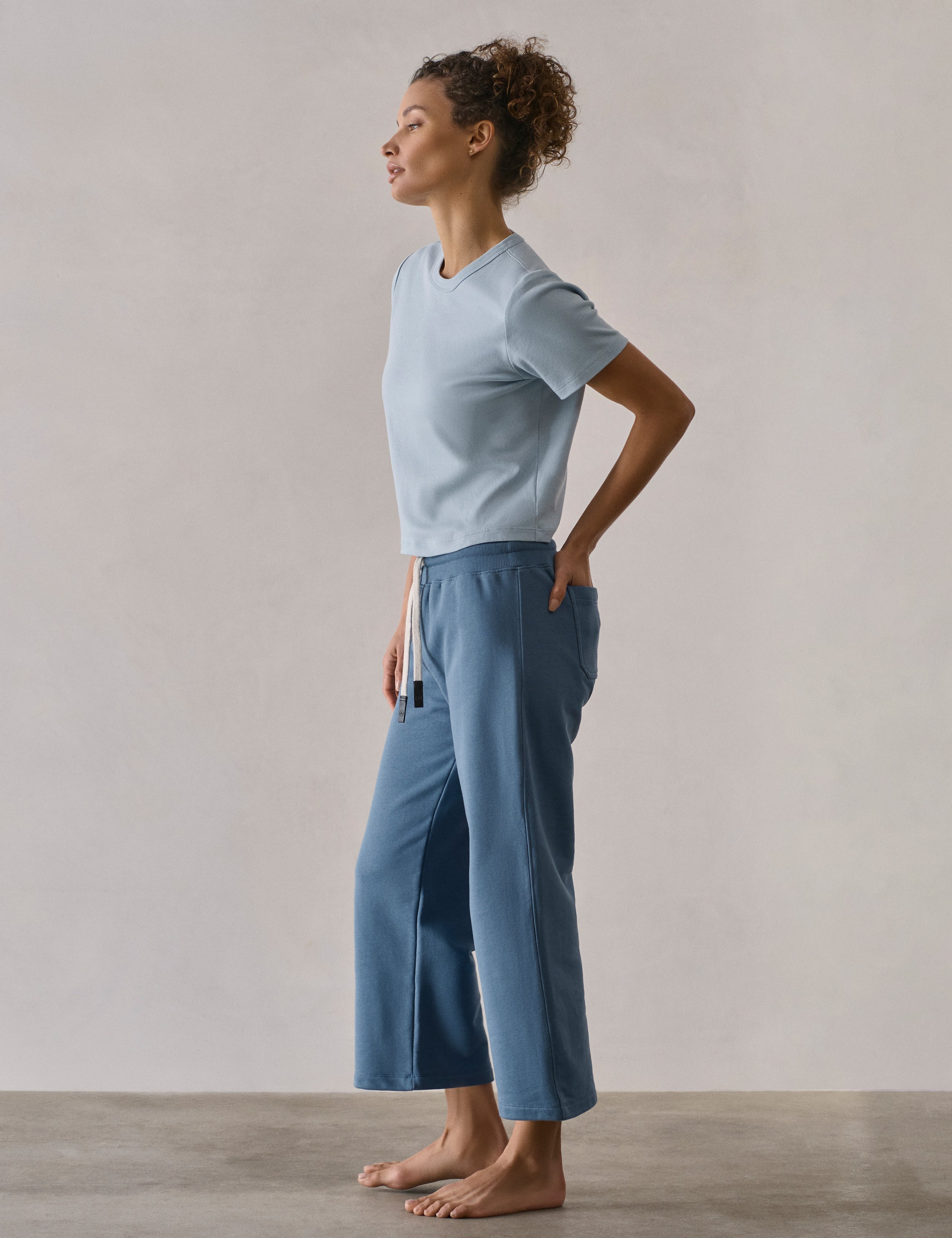 Left side profile full-body view of woman wearing W Osa Cropped Sweatpant in Coastal Blue from AETHER Apparel.