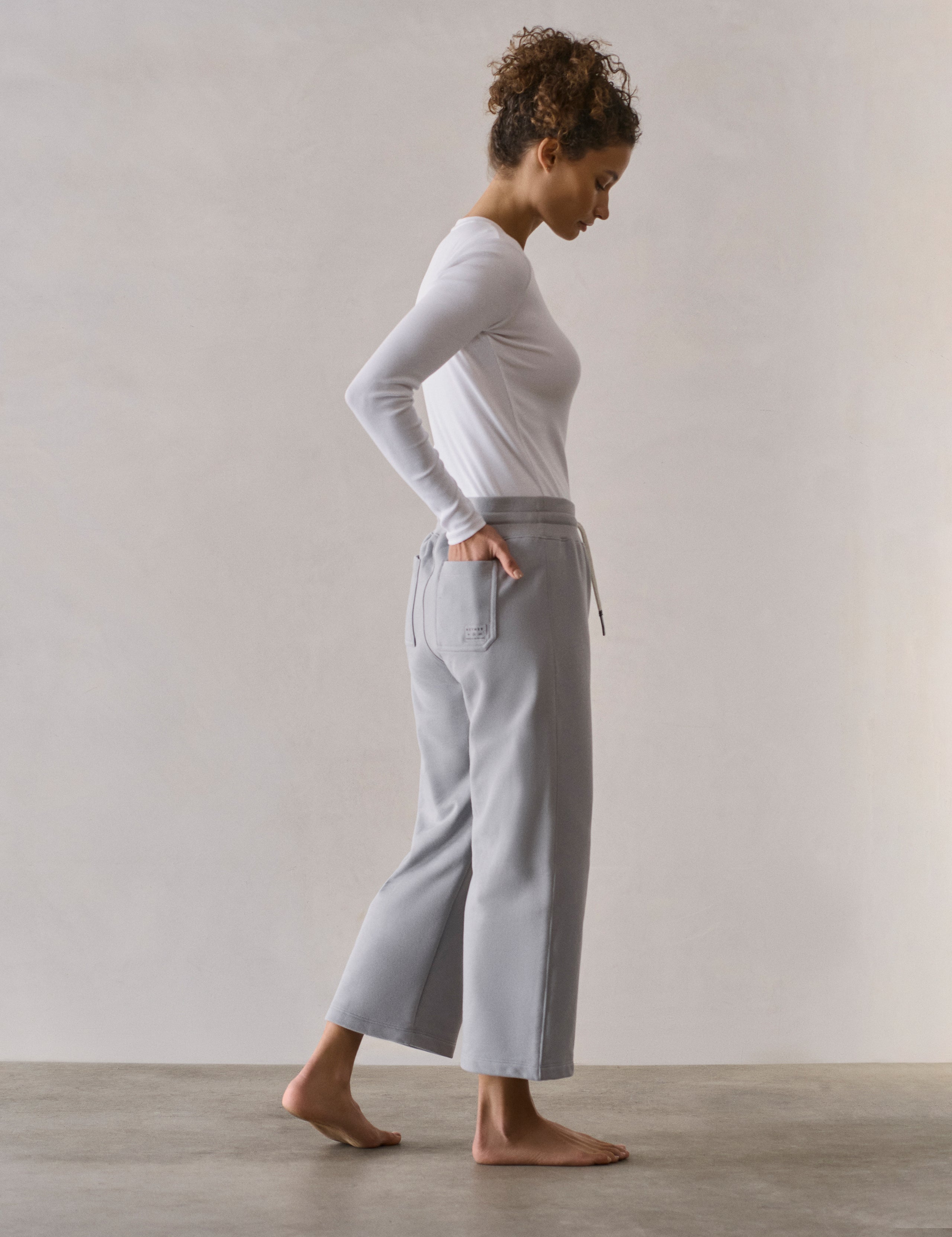 Right side profile full-body view of woman wearing W Osa Cropped Sweatpant in Sky Grey from AETHER Apparel.