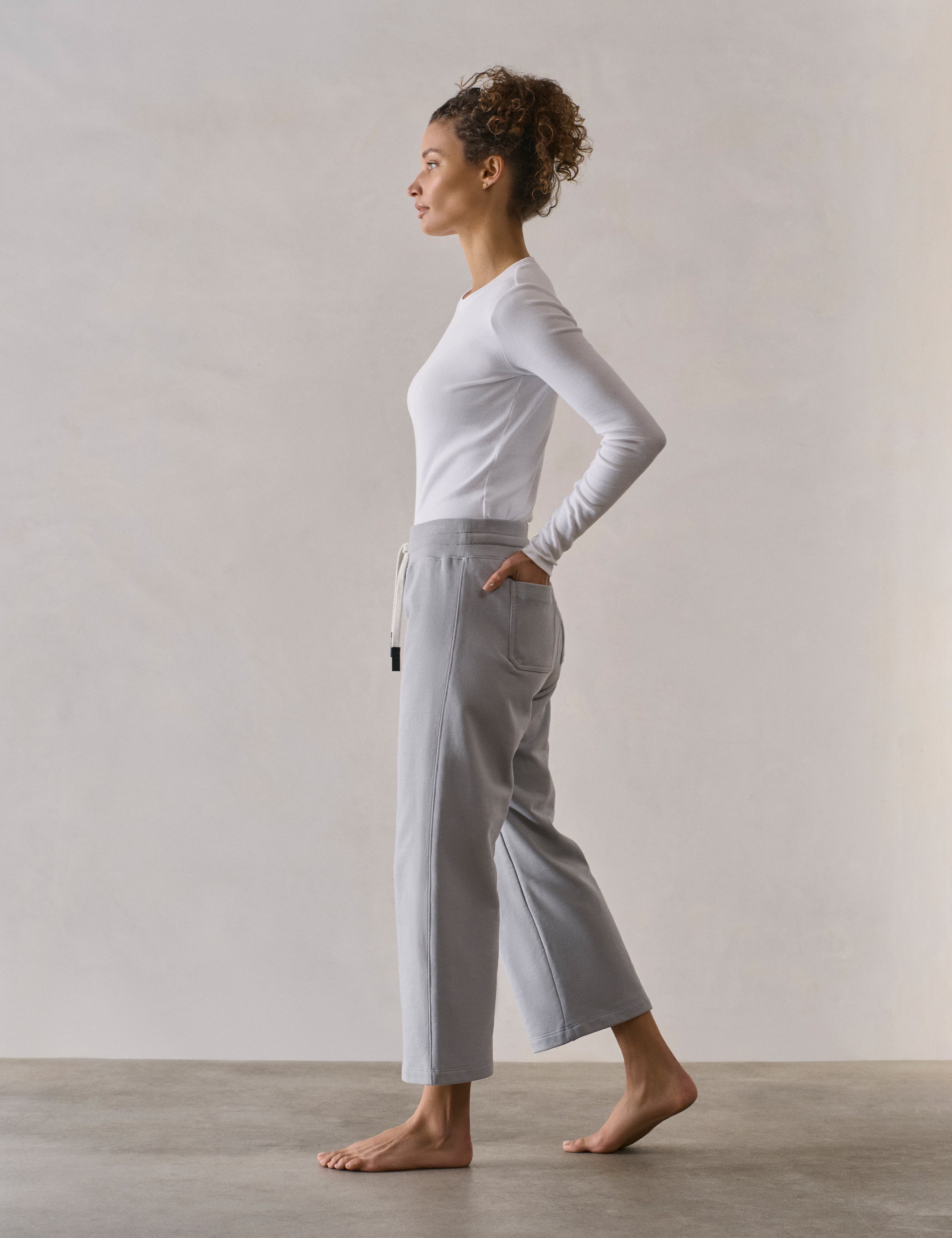 Left side profile full-body view of woman wearing W Osa Cropped Sweatpant in Sky Grey from AETHER Apparel.