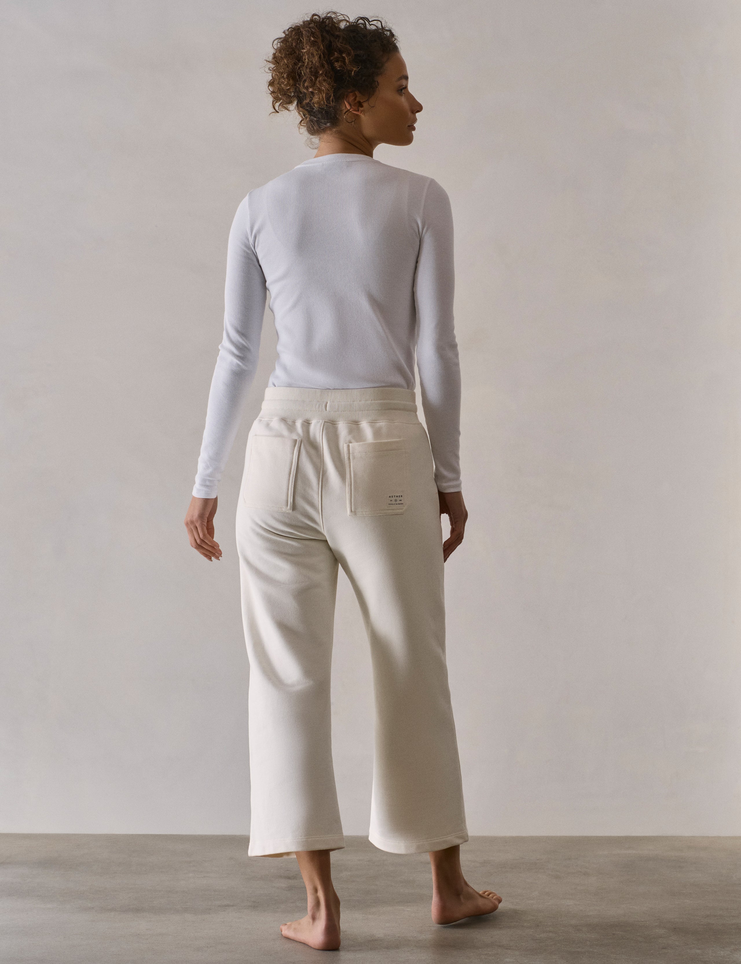 Rear full-body view of woman wearing W Osa Cropped Sweatpant in Winter White from AETHER Apparel.