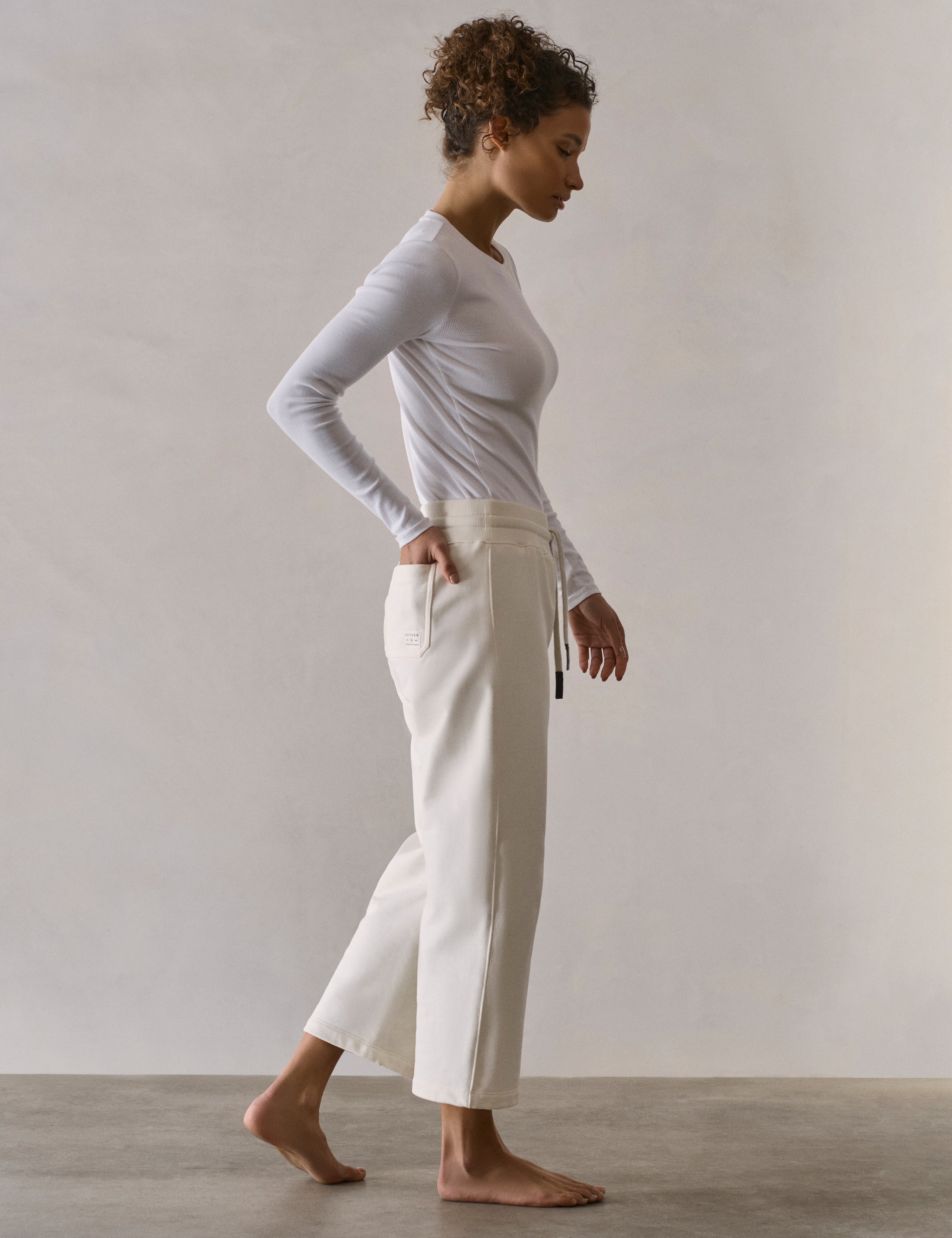 Side profile full-body view of woman wearing W Osa Cropped Sweatpant in Winter White from AETHER Apparel.