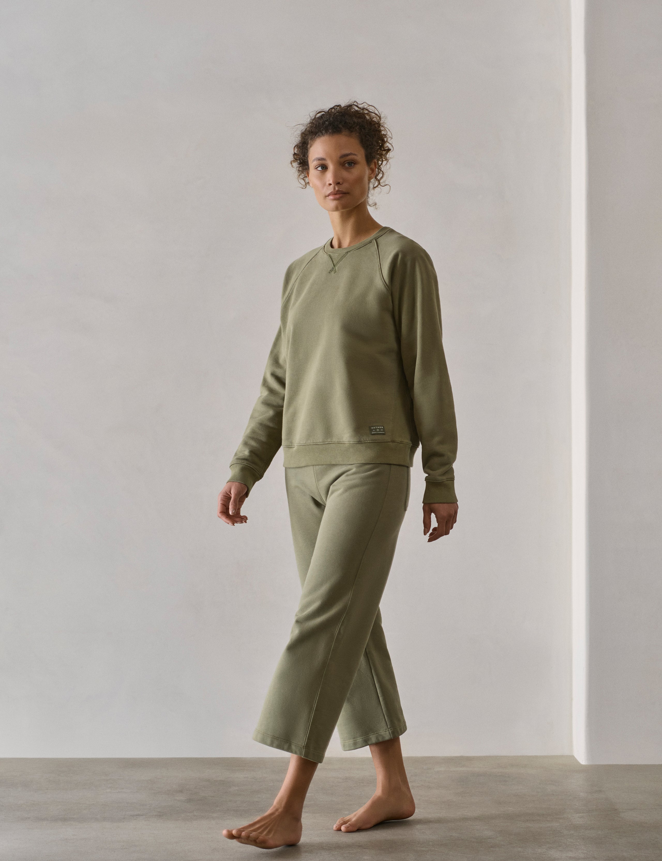 Front 3/4 full-body view of woman walking wearing W Osa Raglan Sweatshirt in Fern Green from AETHER Apparel.