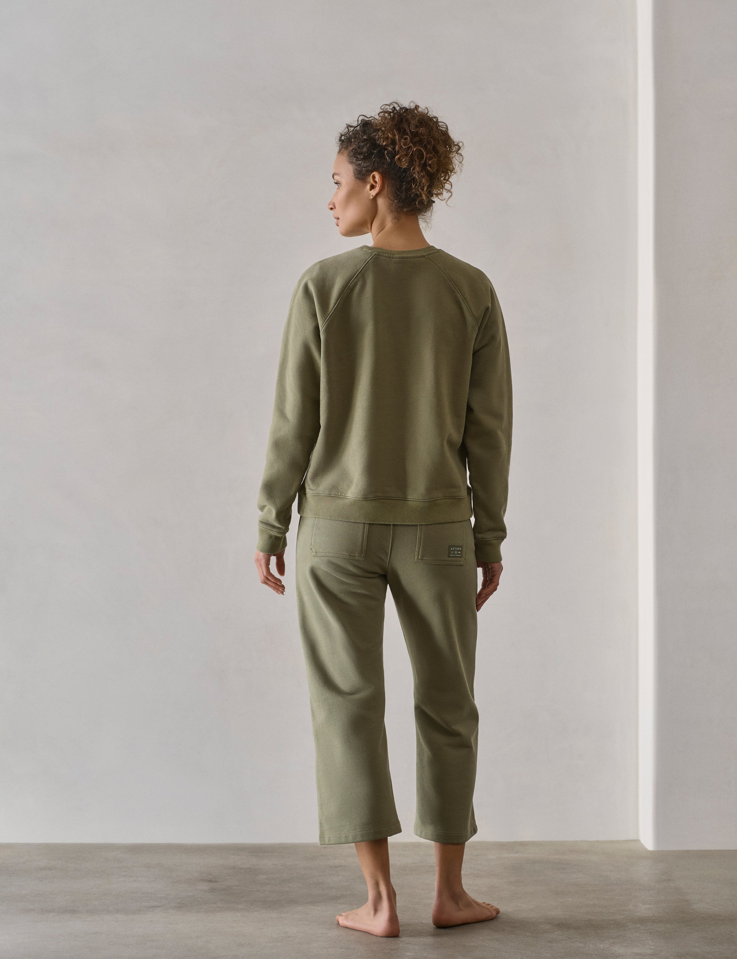 Rear full-body view of woman walking wearing W Osa Raglan Sweatshirt in Fern Green from AETHER Apparel.