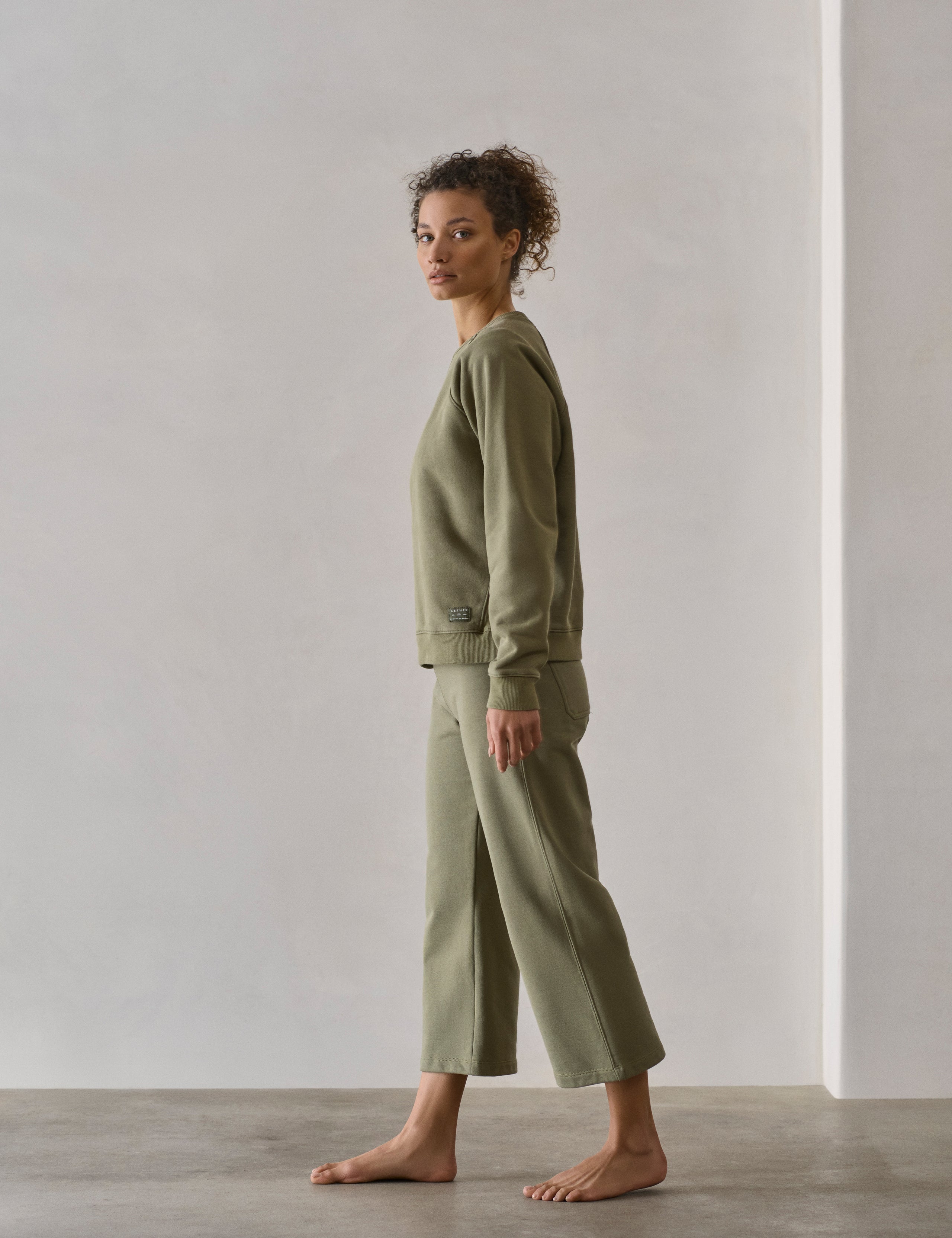 Side profile full-body view of woman walking wearing W Osa Raglan Sweatshirt in Fern Green from AETHER Apparel.