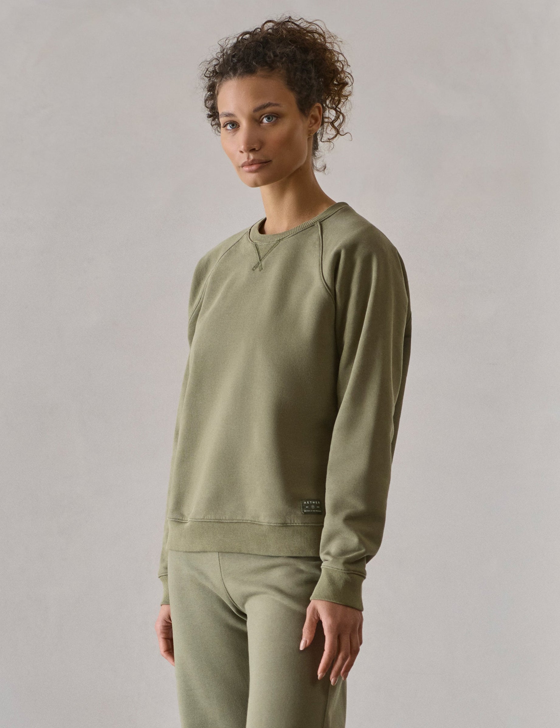 Front 3/4 full-body view of woman standing wearing W Osa Raglan Sweatshirt in Fern Green from AETHER Apparel.